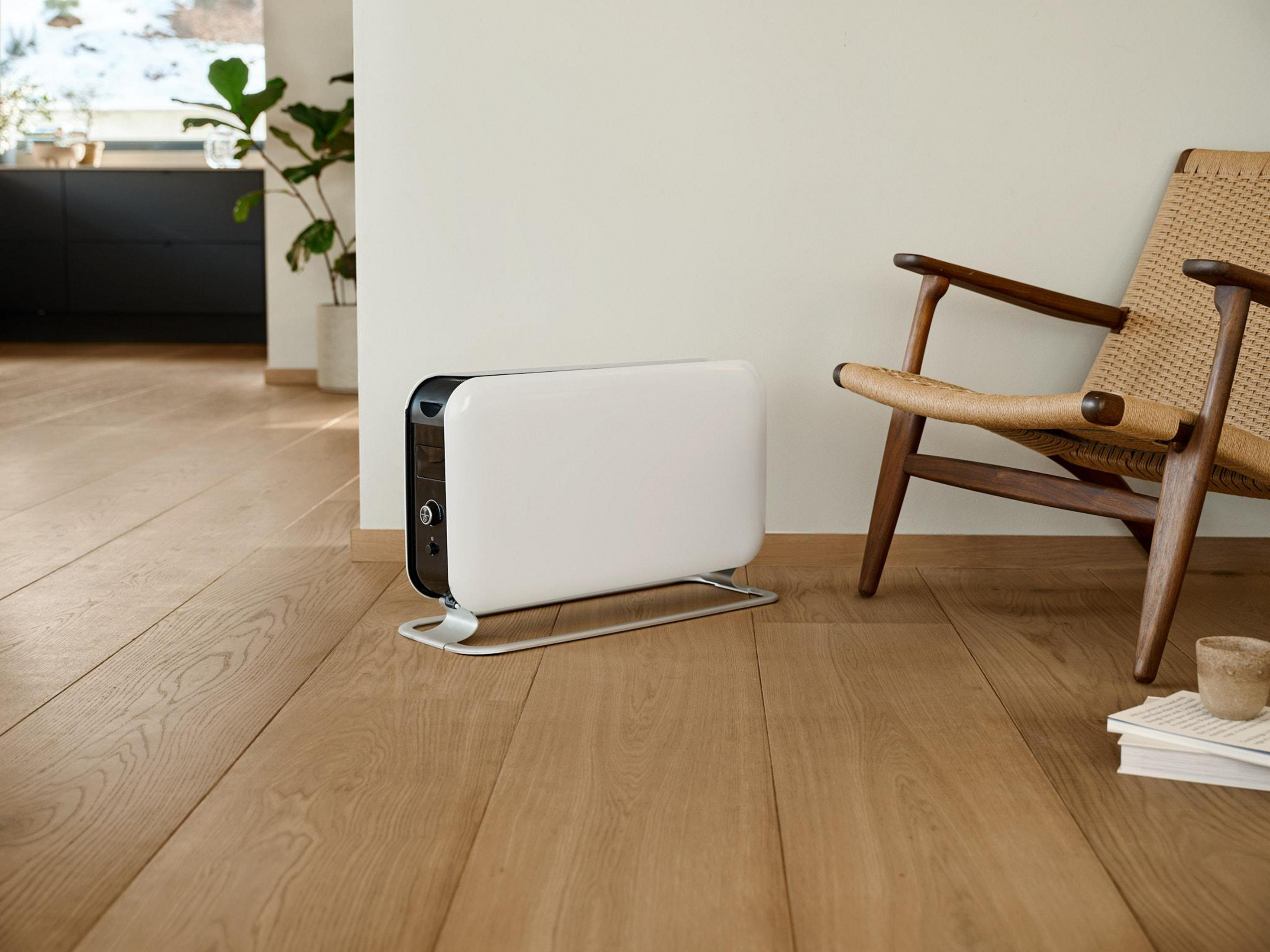 Un radiador blanco está en un suelo de madera junto a un sillón de mimbre.