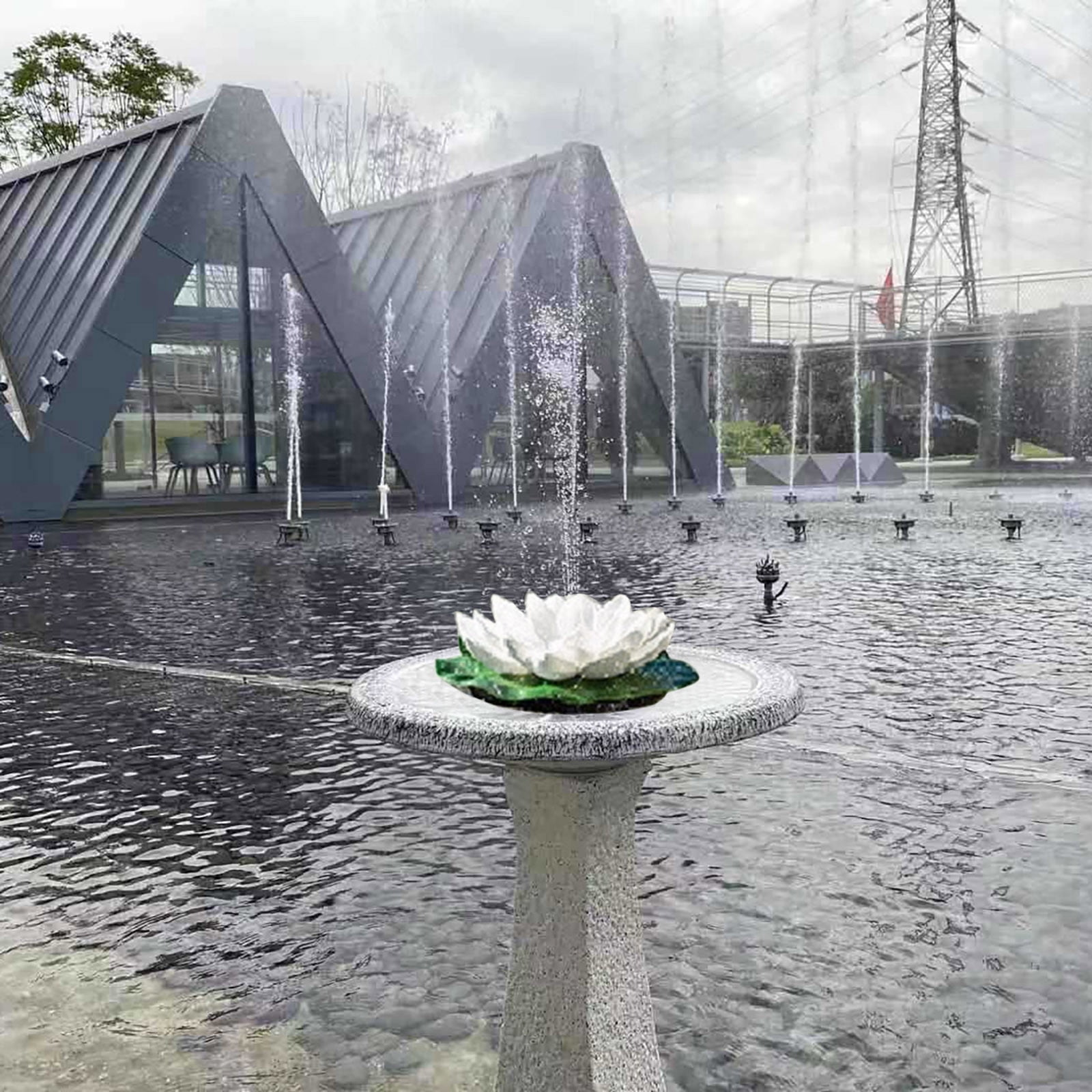 Eine weiße Lotusblumen-Dekoration steht auf einem Sockel in einem Brunnen mit Wasserstrahlen.