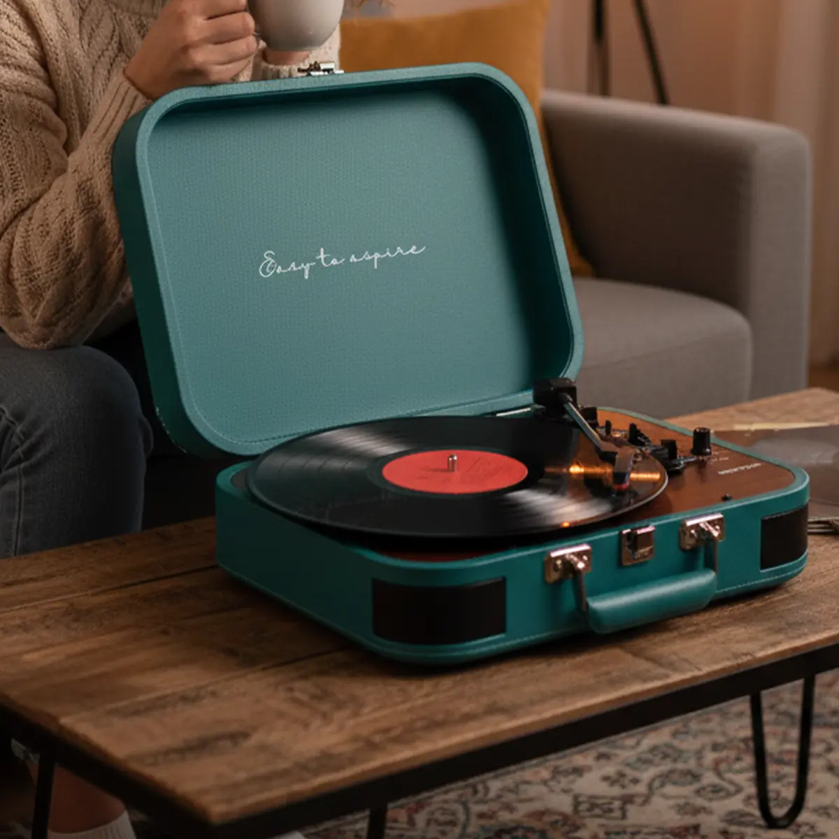 Tealowy gramofon walizka z płytą winylową i osoba trzymająca kubek.