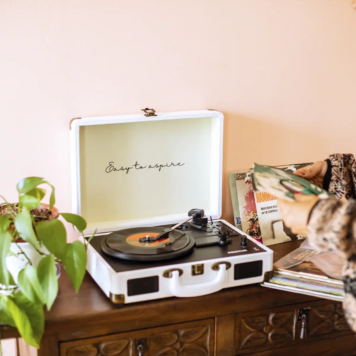 Gramofon walizkowy z płytą winylową, obok stos płyt.