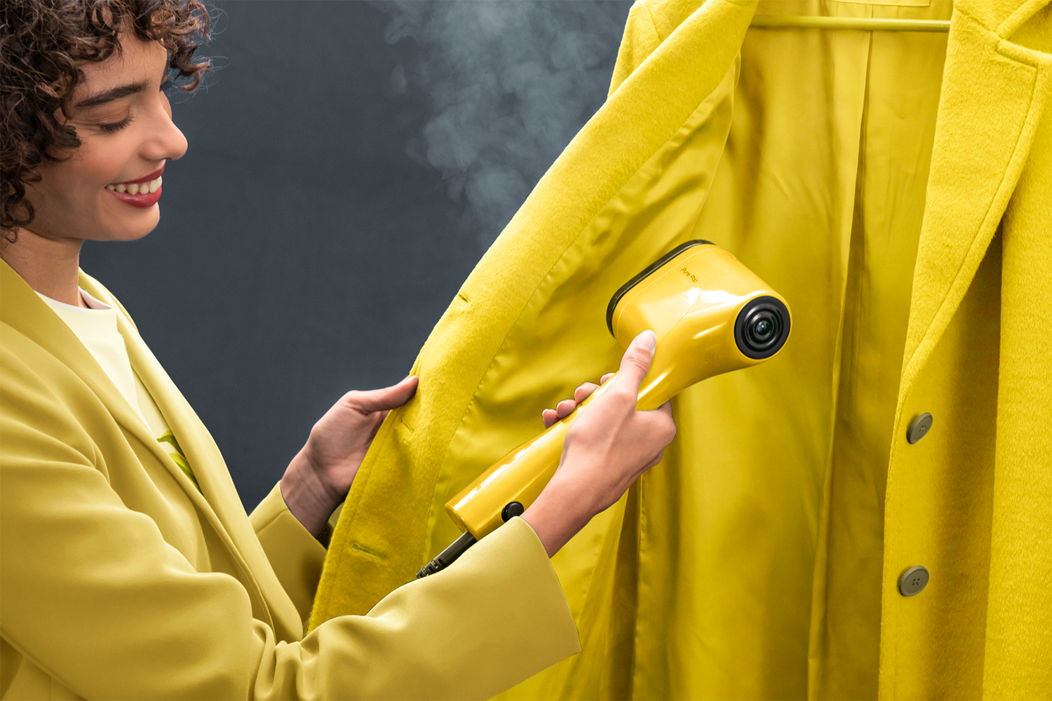 Donna stira cappotto giallo con vaporizzatore. Sale vapore.