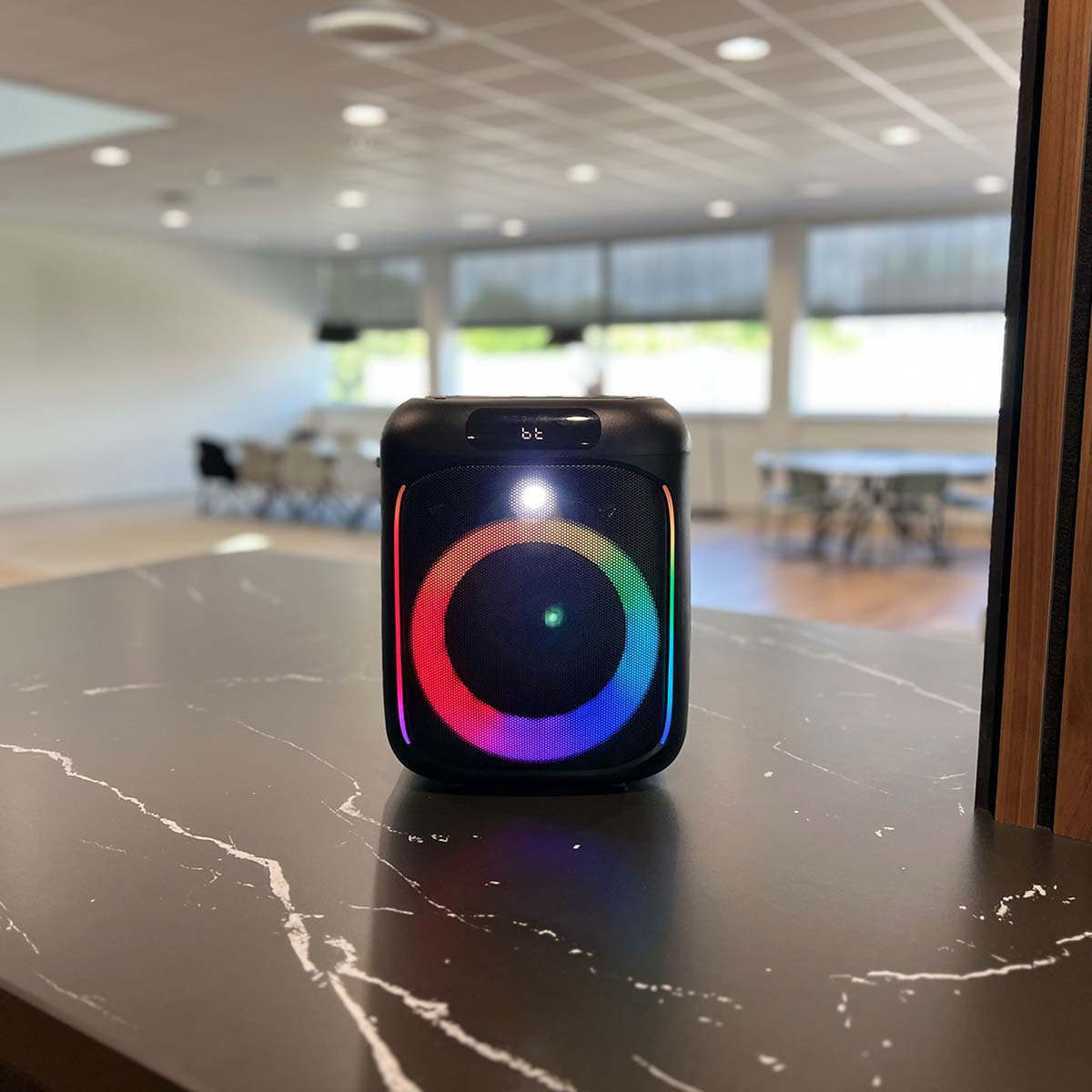 Ein schwarzer Bluetooth-Lautsprecher mit einem bunten Lichtring steht auf einer Marmorplatte.