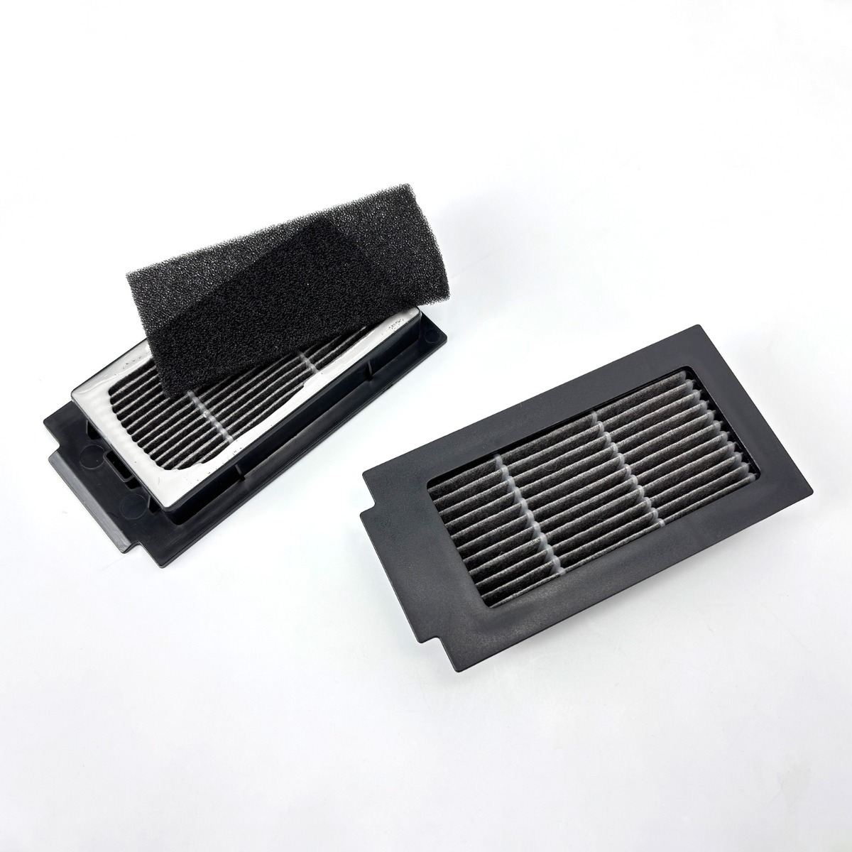 Dwa czarne ramki filtrów powietrza z szarymi filtrami i jednym filtrem gąbkowym na białym.