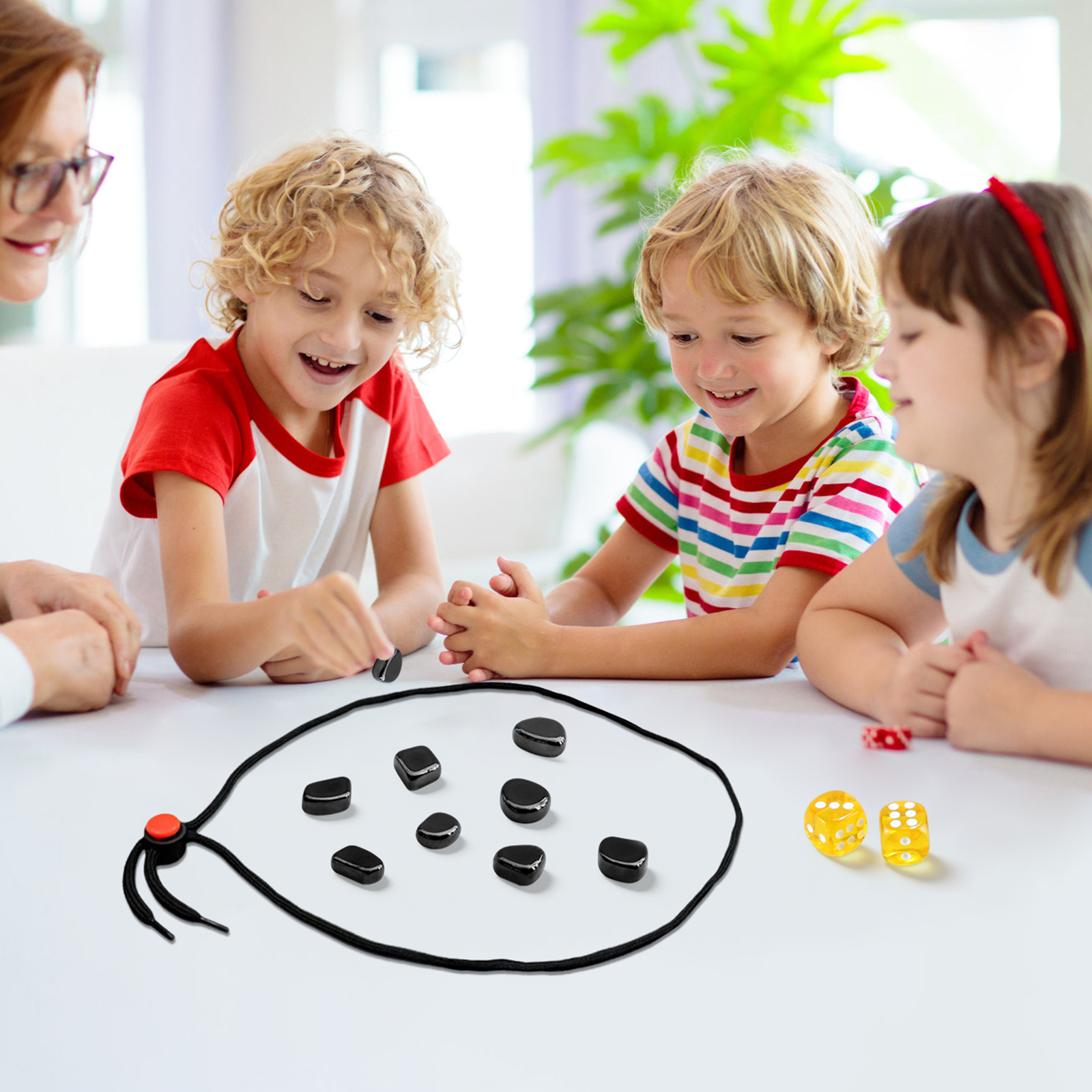 Kinder spielen Brettspiel mit schwarzen Steinen, Würfeln und Schnur auf weißem Tisch.