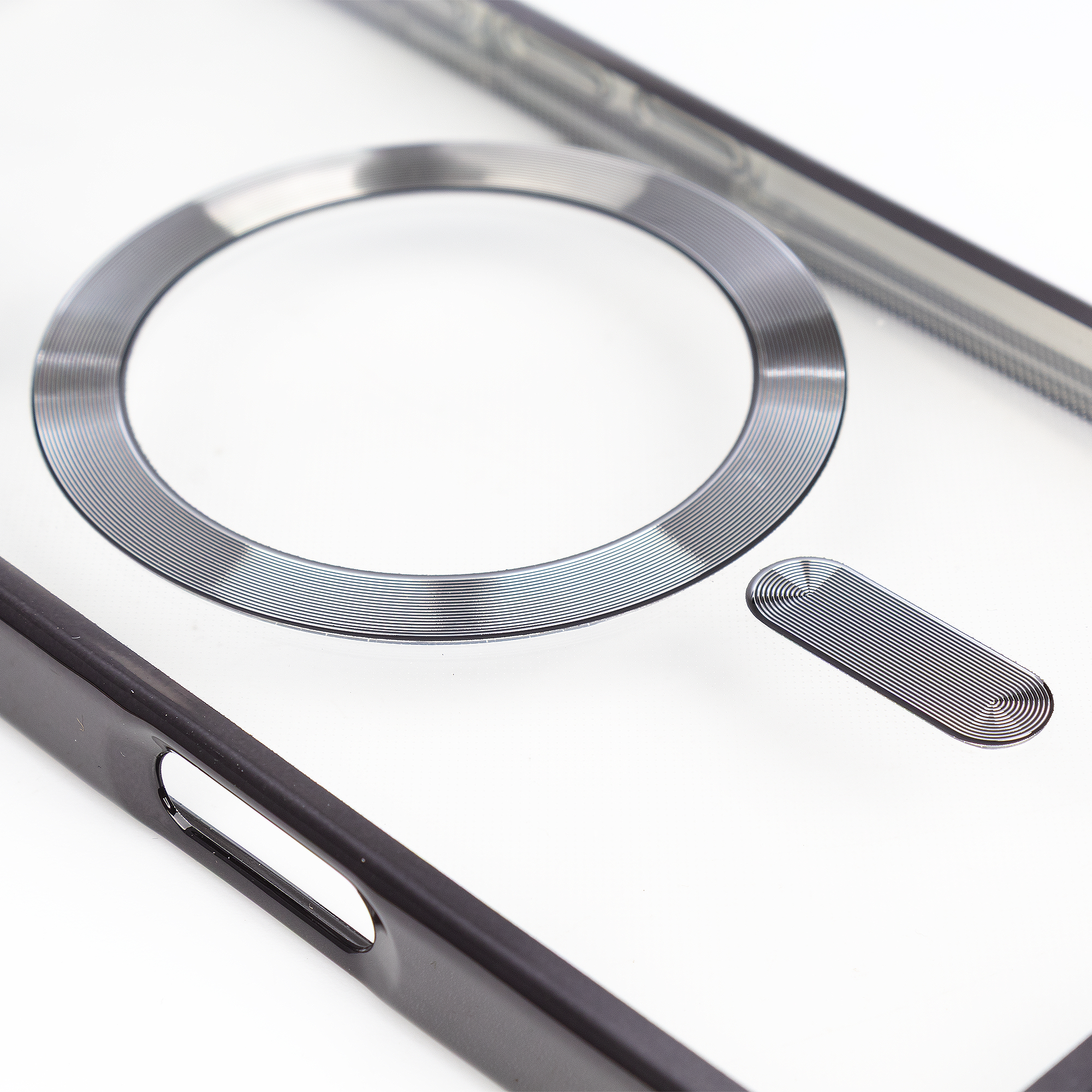 Un anello argentato e un elemento ovale con linee concentriche su sfondo bianco.