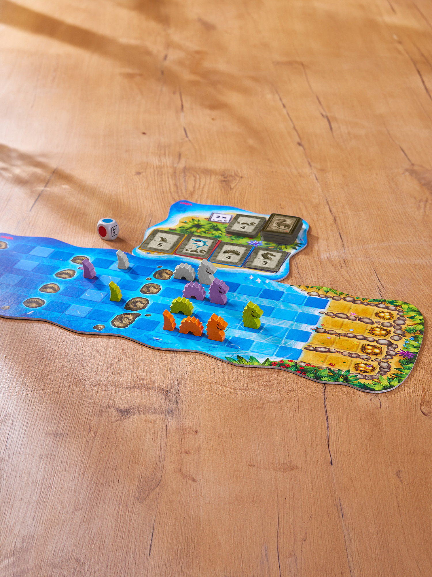Ein Würfel und bunte Spielfiguren auf einem Brettspiel mit Wasser- und Inselmotiven.