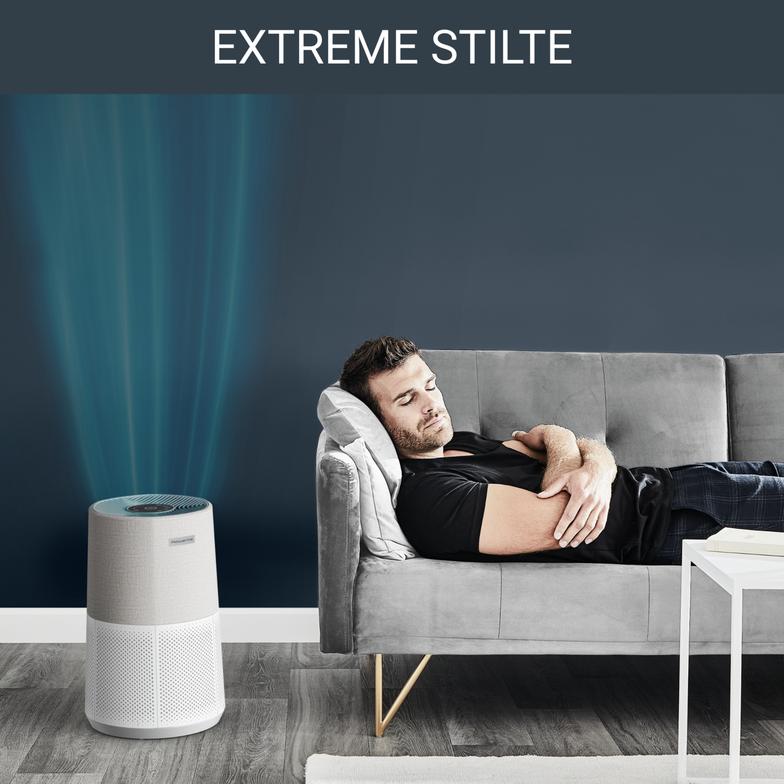 Ein Mann schläft auf einem Sofa, während ein Luftreiniger mit blauen Strahlen daneben steht.
