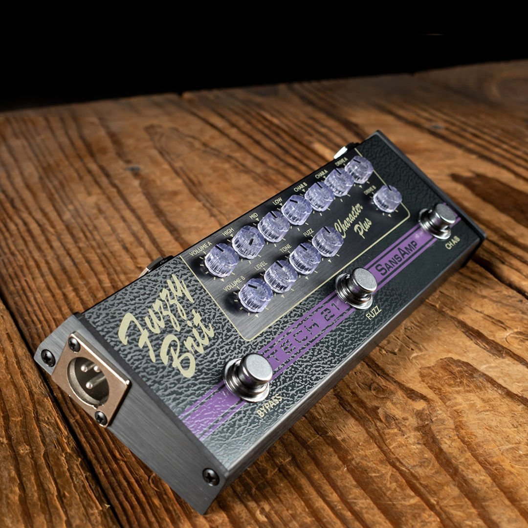 Çok sayıda düğme ve anahtara sahip siyah bir SansAmp gitar pedalı ahşap bir yüzeyde duruyor.