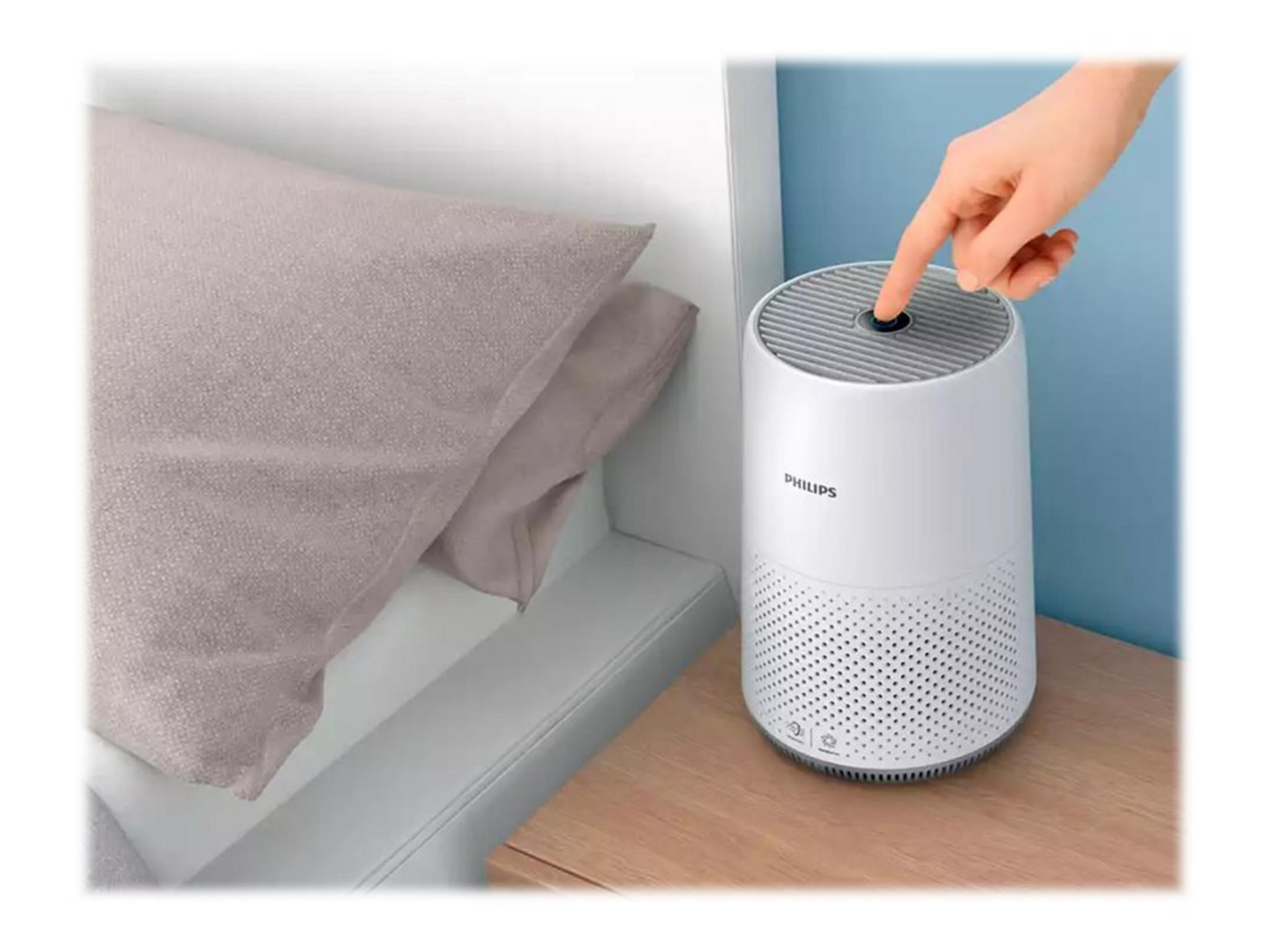 Una mano preme un pulsante su un purificatore d'aria Philips bianco accanto a un cuscino.