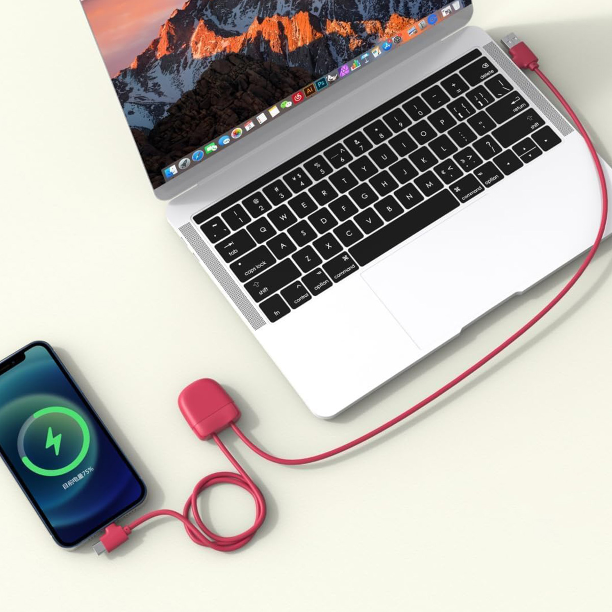 Un cavo di ricarica rosso collega un telefono e un laptop. Il telefono mostra il 75% di carica.