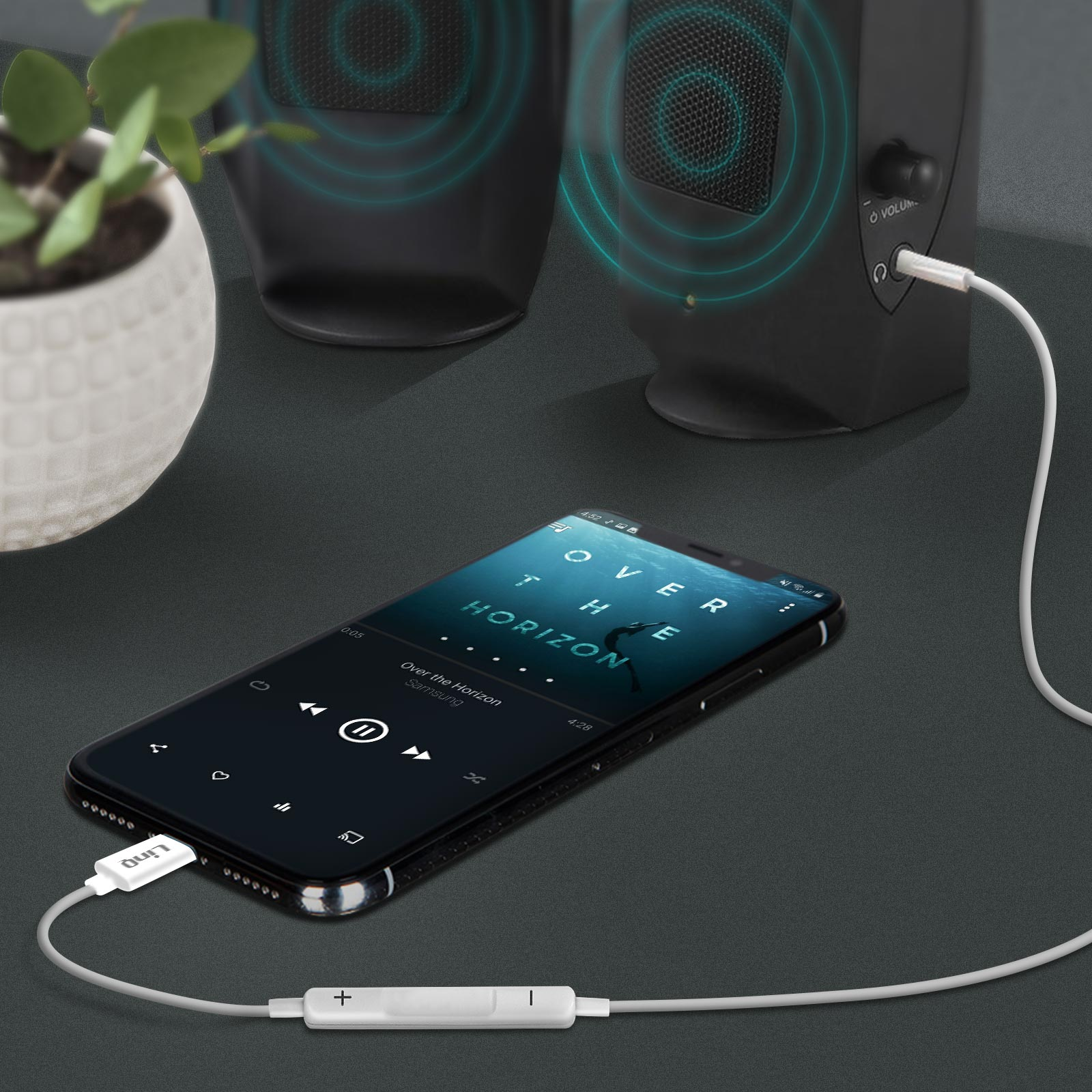 Uno smartphone riproduce musica tramite altoparlanti, collegato da un cavo.