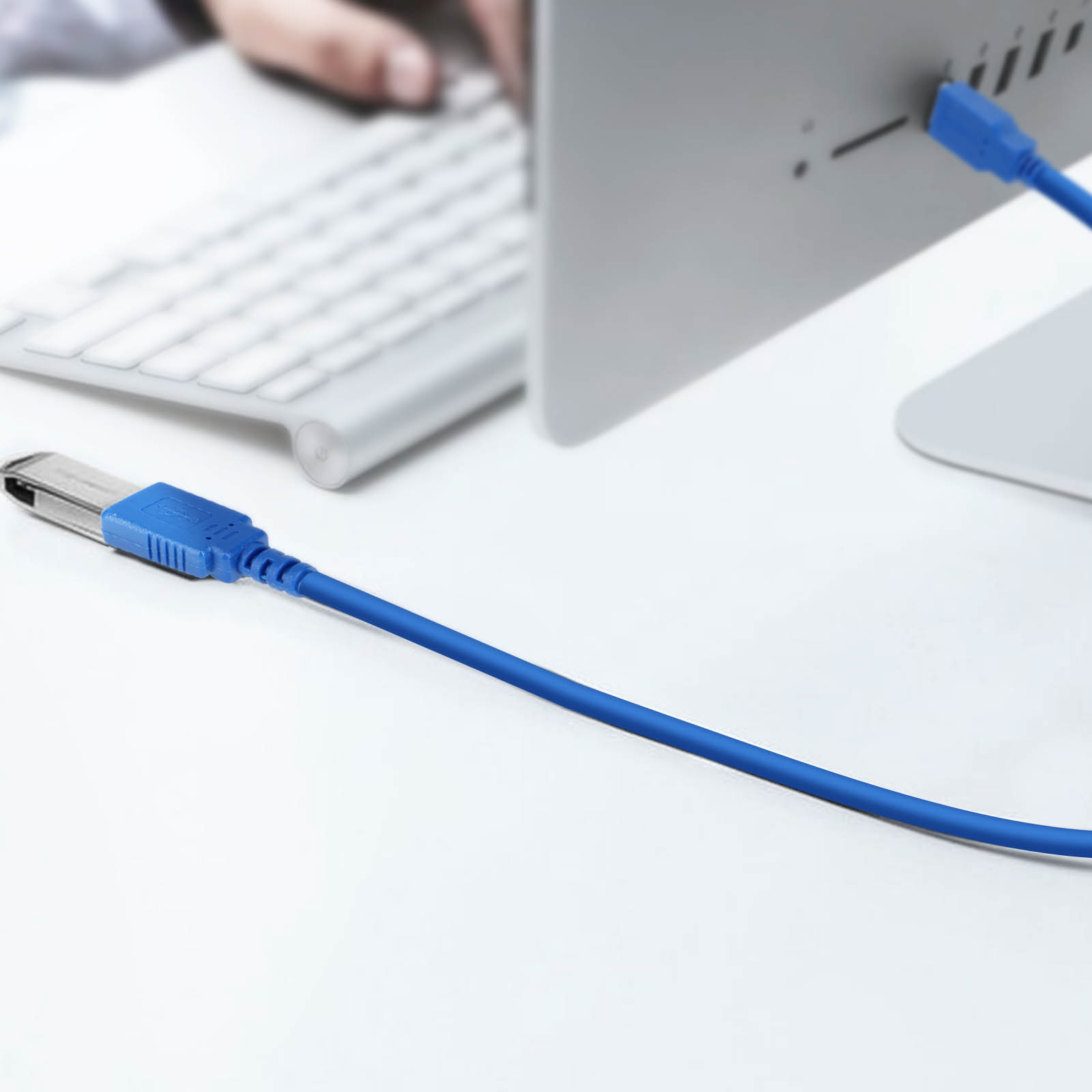 Un cavo USB blu è collegato a un computer, con una tastiera nelle vicinanze.