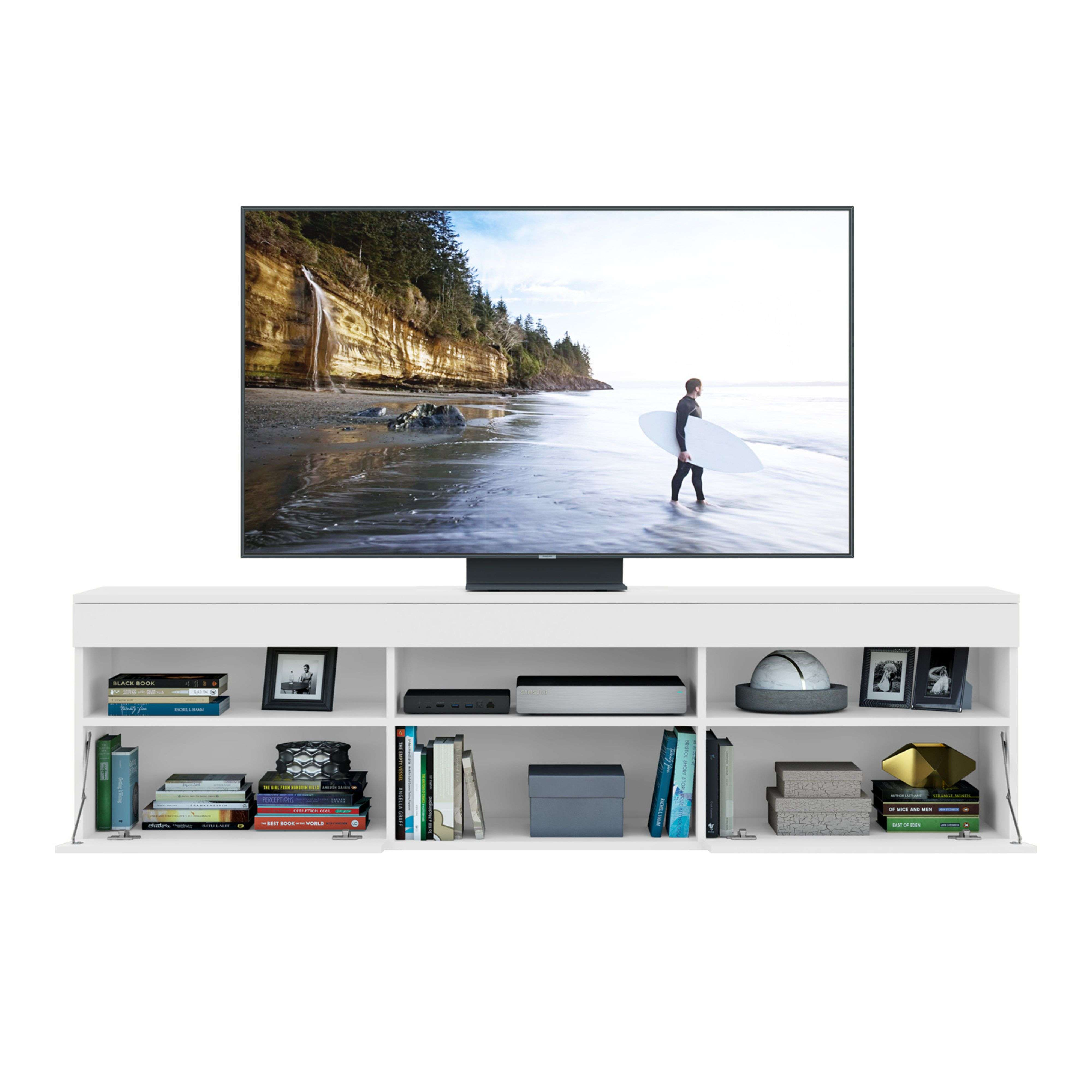 Una consola multimedia blanca con TV mostrando una costa. Debajo hay libros, decoración y aparatos.