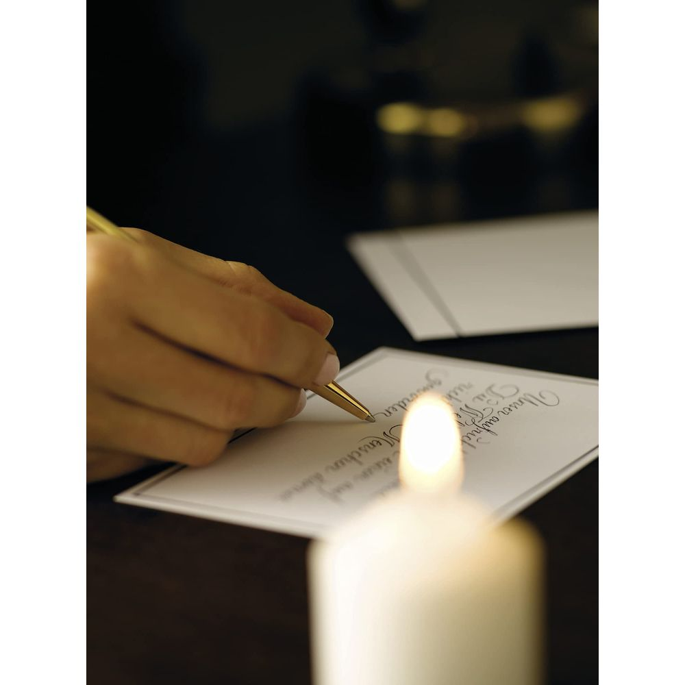 Eine Hand schreibt mit einem goldenen Stift auf eine Karte, beleuchtet von einer Kerze.
