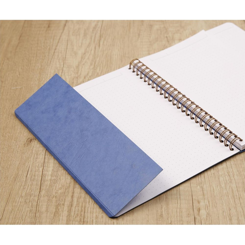 Ein blauer Einband liegt auf einem geöffneten Notizbuch mit Spiralbindung.