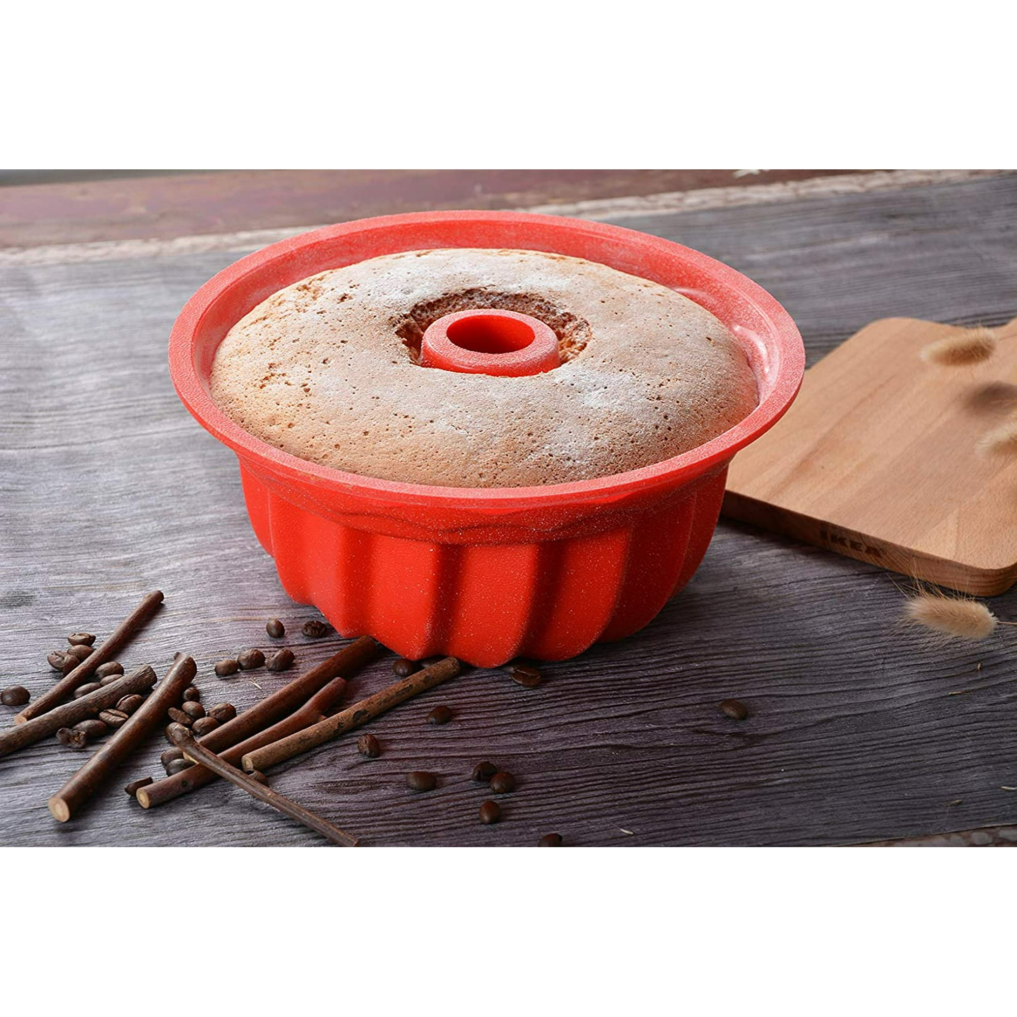 Ein runder Kuchen in roter Silikonform auf Holztisch mit Kaffeebohnen und Stöcken.