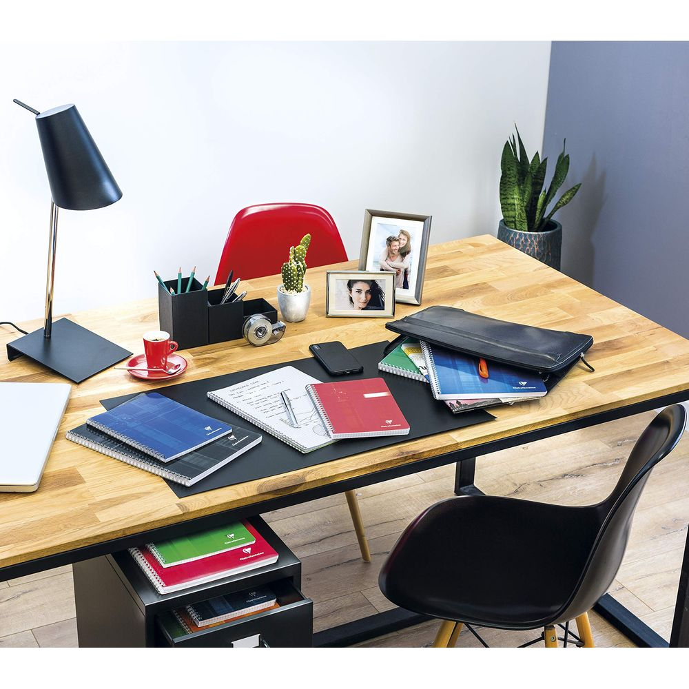 Un bureau en bois avec une lampe noire, des carnets, des cadres photo et une chaise noire.