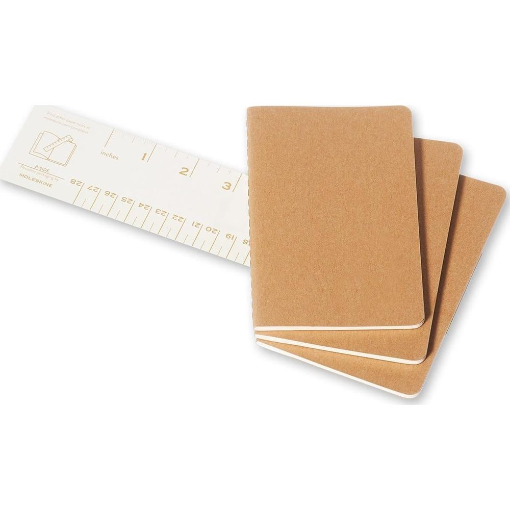 Trois carnets Moleskine marron et une règle avec des marques en pouces et en cm sur fond blanc.