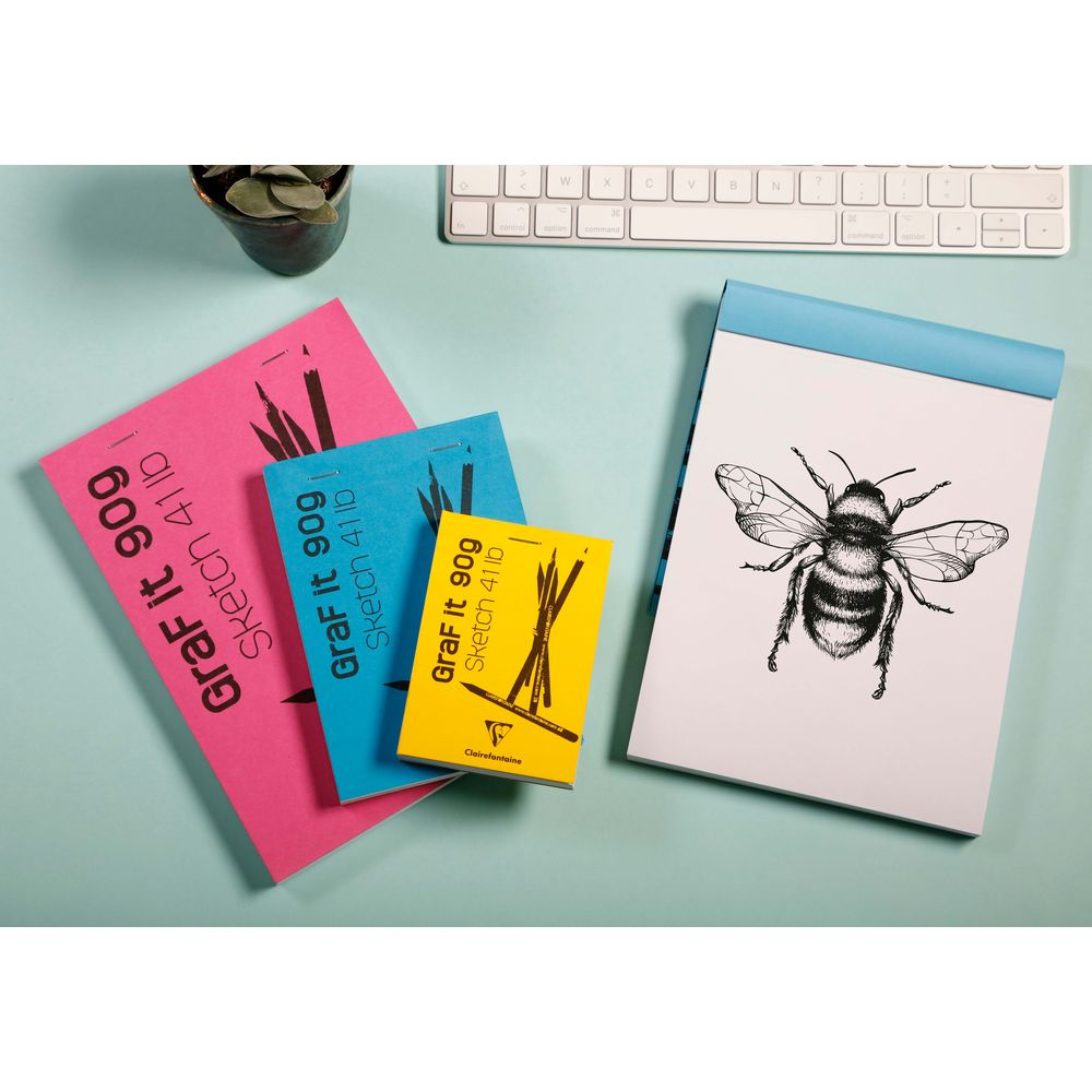Skizzenbuch mit Bienenzeichnung, bunte Notizblöcke und Tastatur.
