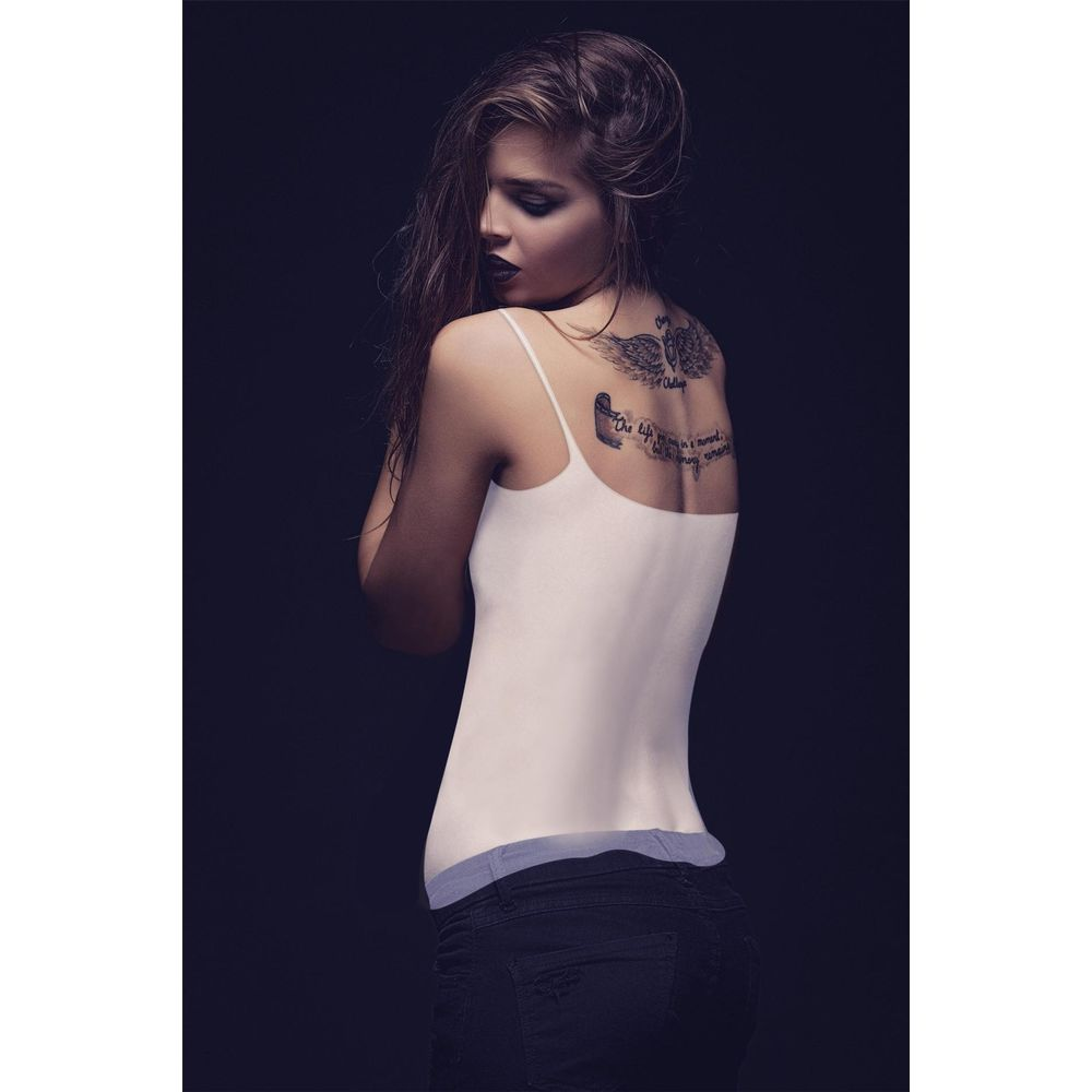 Donna con tatuaggio sulla schiena, indossa un top bianco e jeans neri.