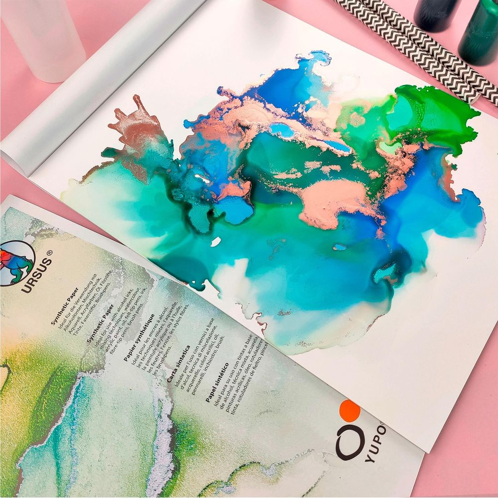 Art abstrait avec de l'encre bleue, verte et rose sur papier, avec pailles et bouteilles en arrière-plan.