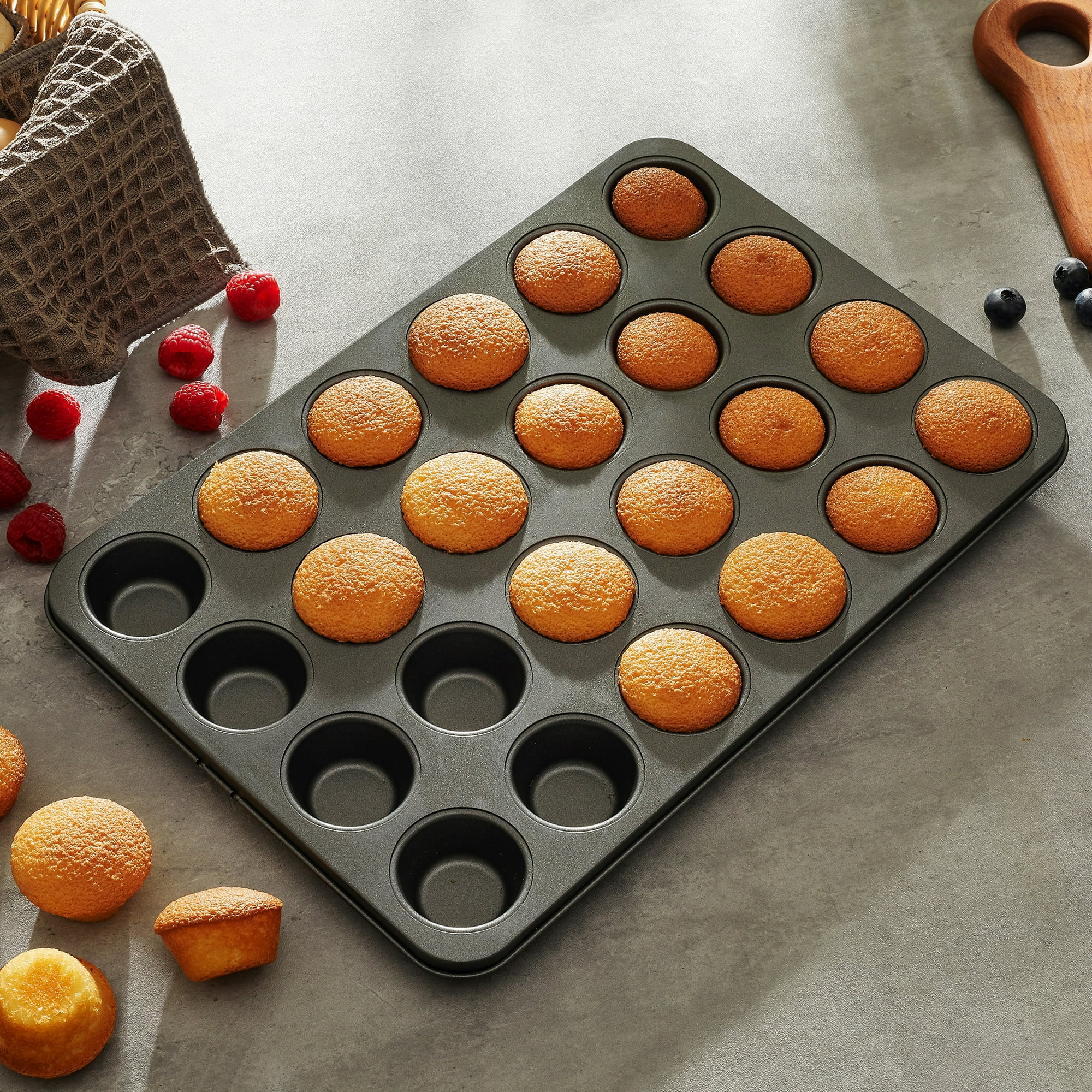 Ein Muffinblech mit gebackenen Muffins, Beeren und einem Handtuch.