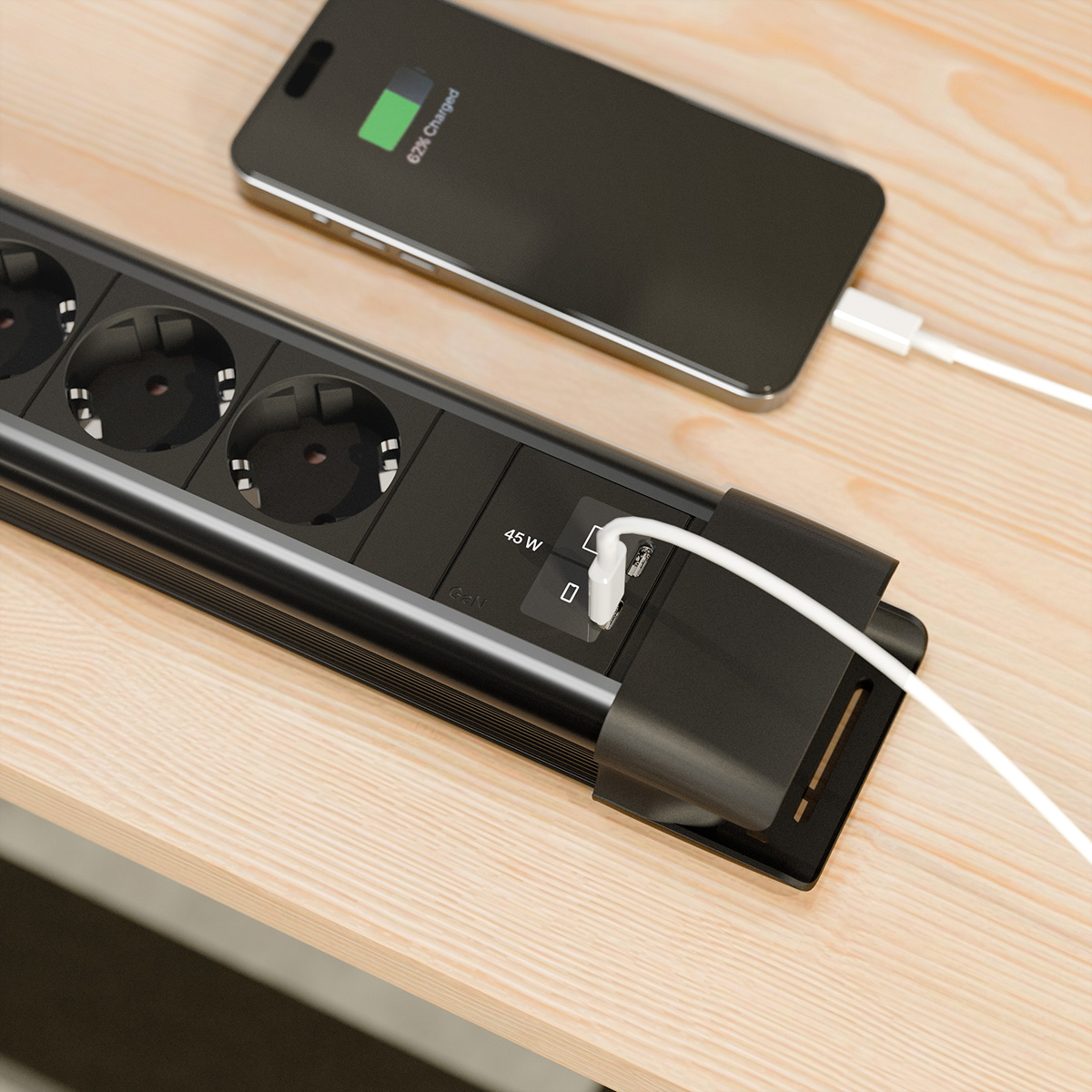 Eine schwarze Steckdosenleiste mit mehreren Steckdosen und USB-Anschlüssen lädt ein Handy auf.