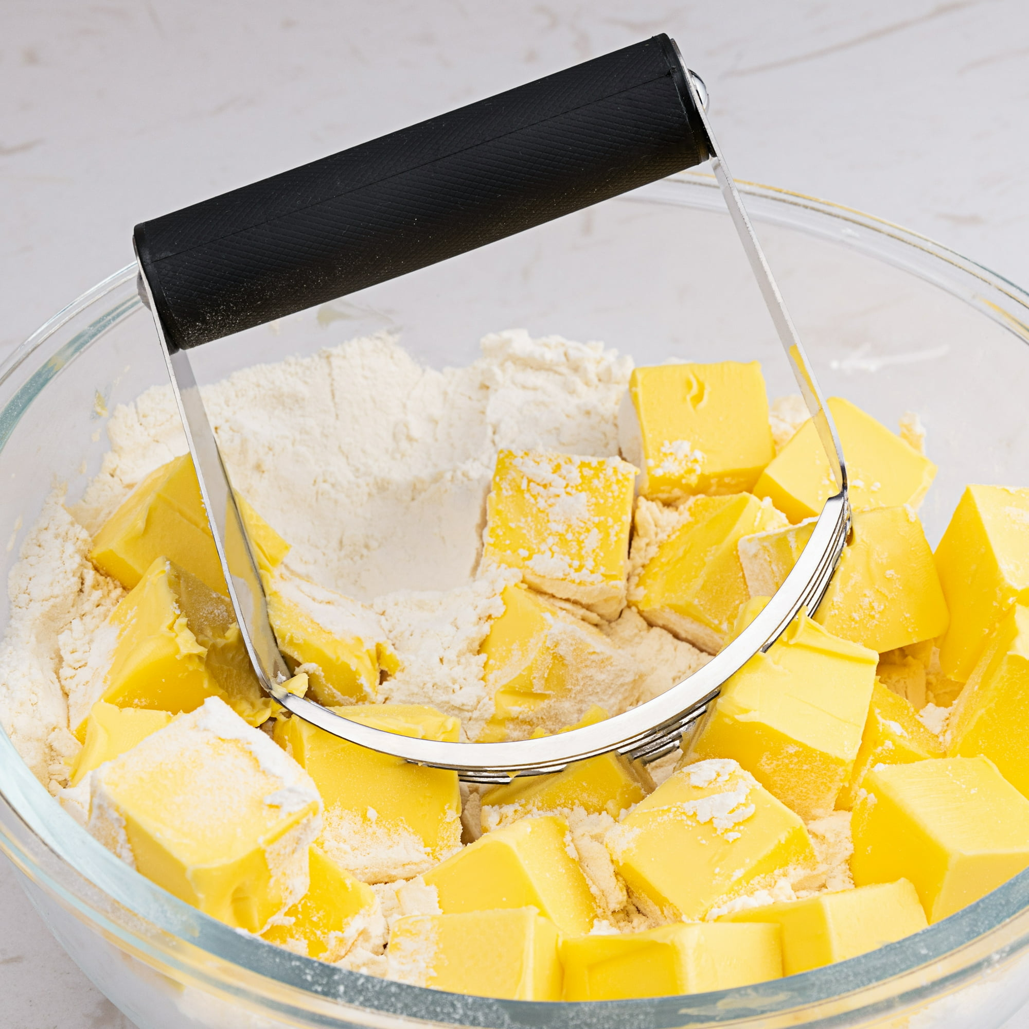 Ein Teigschneider liegt über gewürfelter Butter in einer Schüssel mit Mehl.