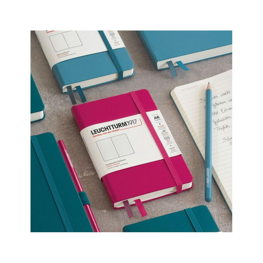 Mehrere Notizbücher in Pink und Blau liegen auf einem Tisch. Ein blauer Stift liegt auf einer geöffneten Seite.