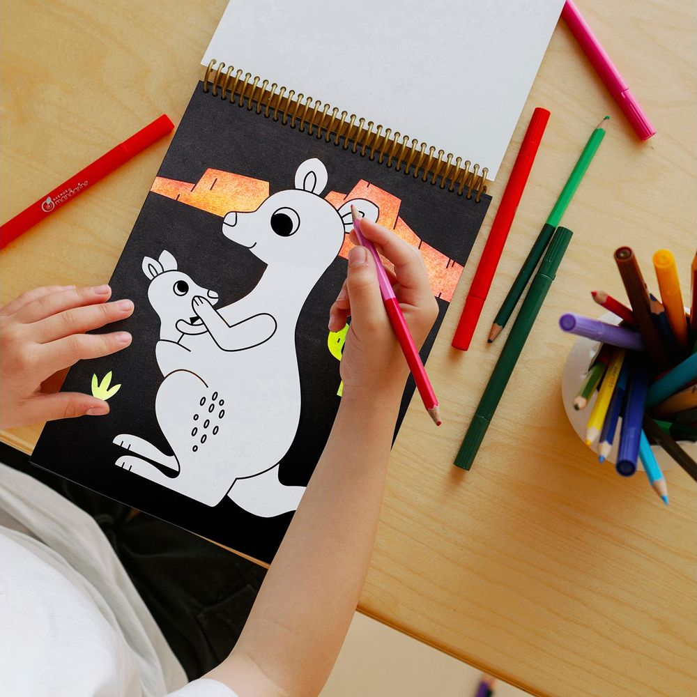 Un bambino colora un canguro e un cucciolo su carta nera con matite colorate.