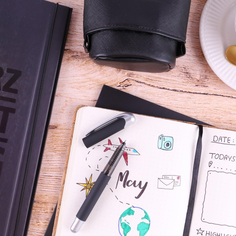 Ein Journal mit Zeichnungen eines Flugzeugs, der Erde und einer Kamera, neben einem Stift.