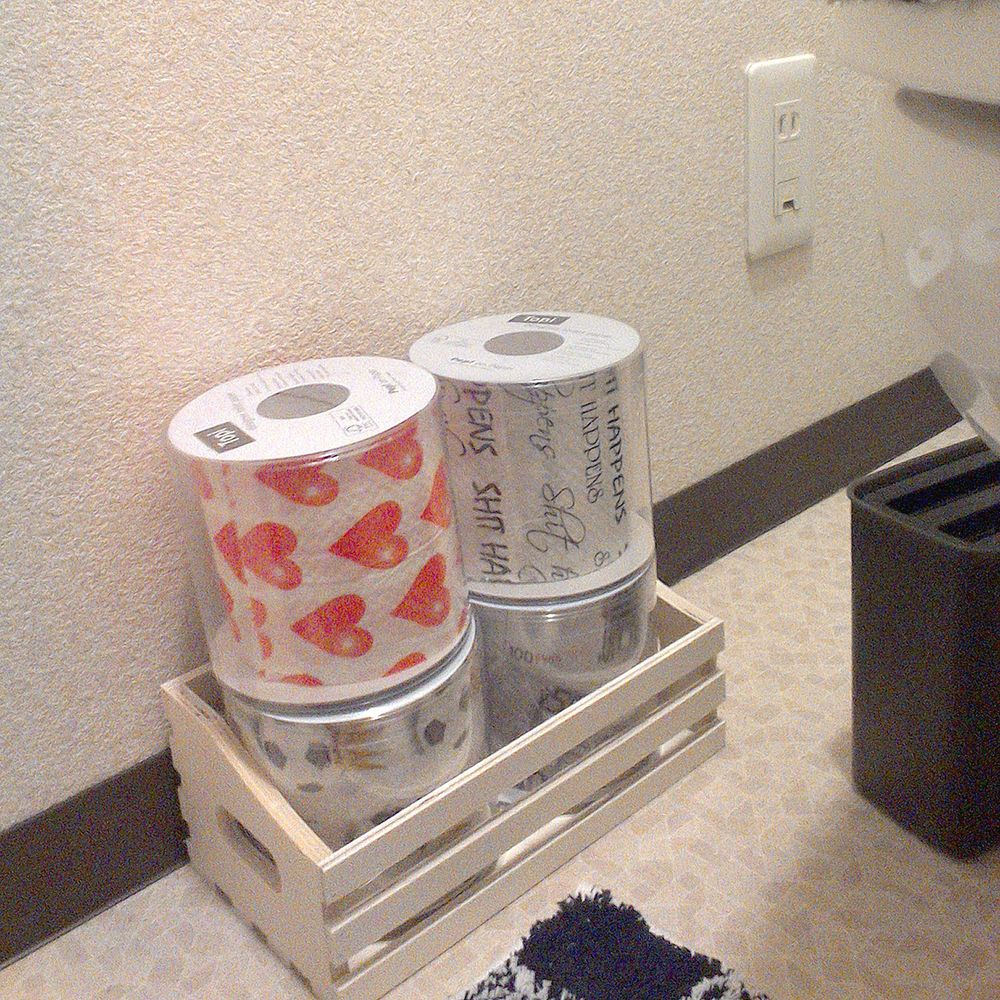 Zwei Toilettenpapierrollen, eine mit roten Herzen, in einer Holzkiste.