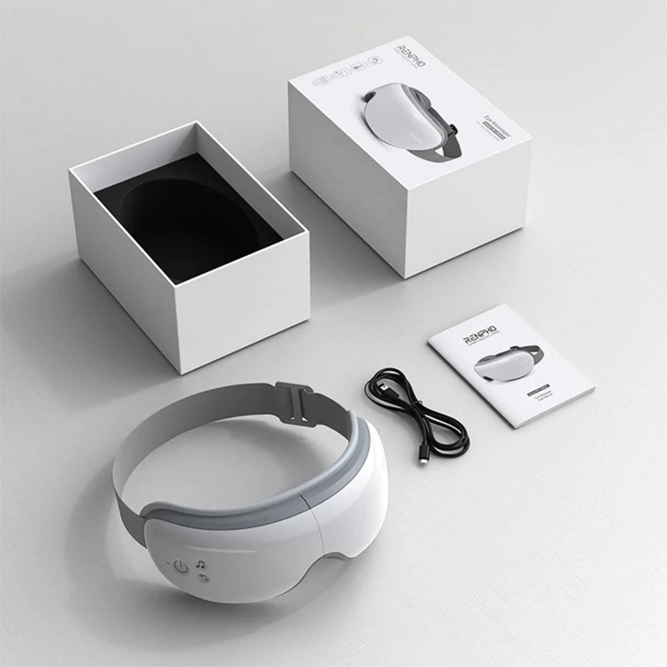 Ein weißer Augenmassager mit grauen Details, Kabel und Anleitung liegen daneben.