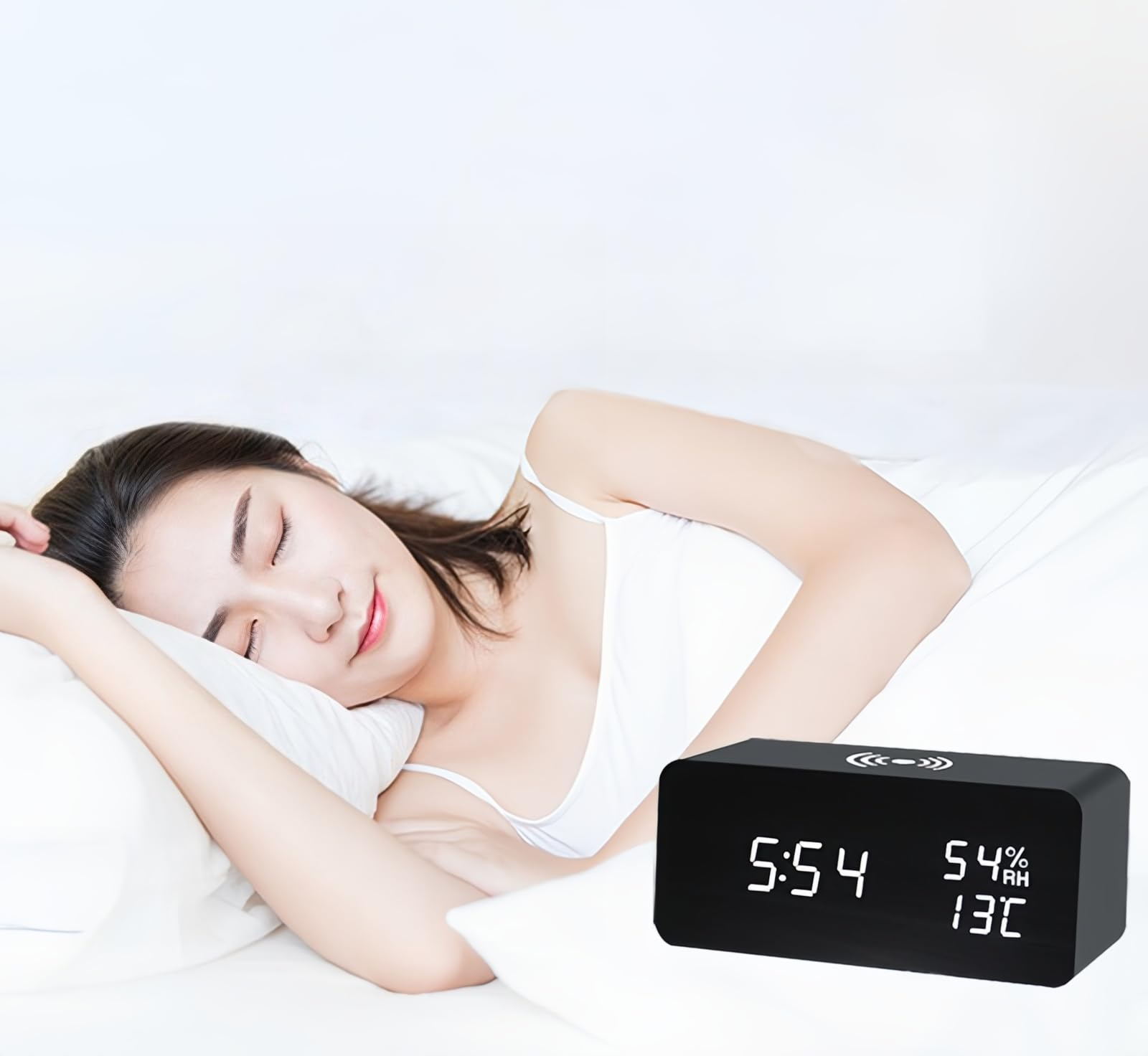 Eine Frau schläft in einem weißen Bett mit einem digitalen Wecker.