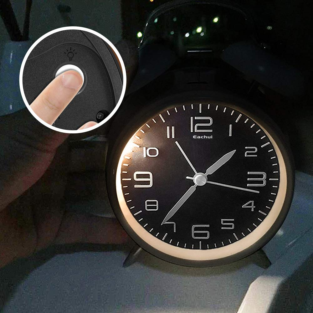 Ein Finger drückt den Lichtknopf einer schwarzen analogen Weckuhr mit beleuchtetem Zifferblatt.