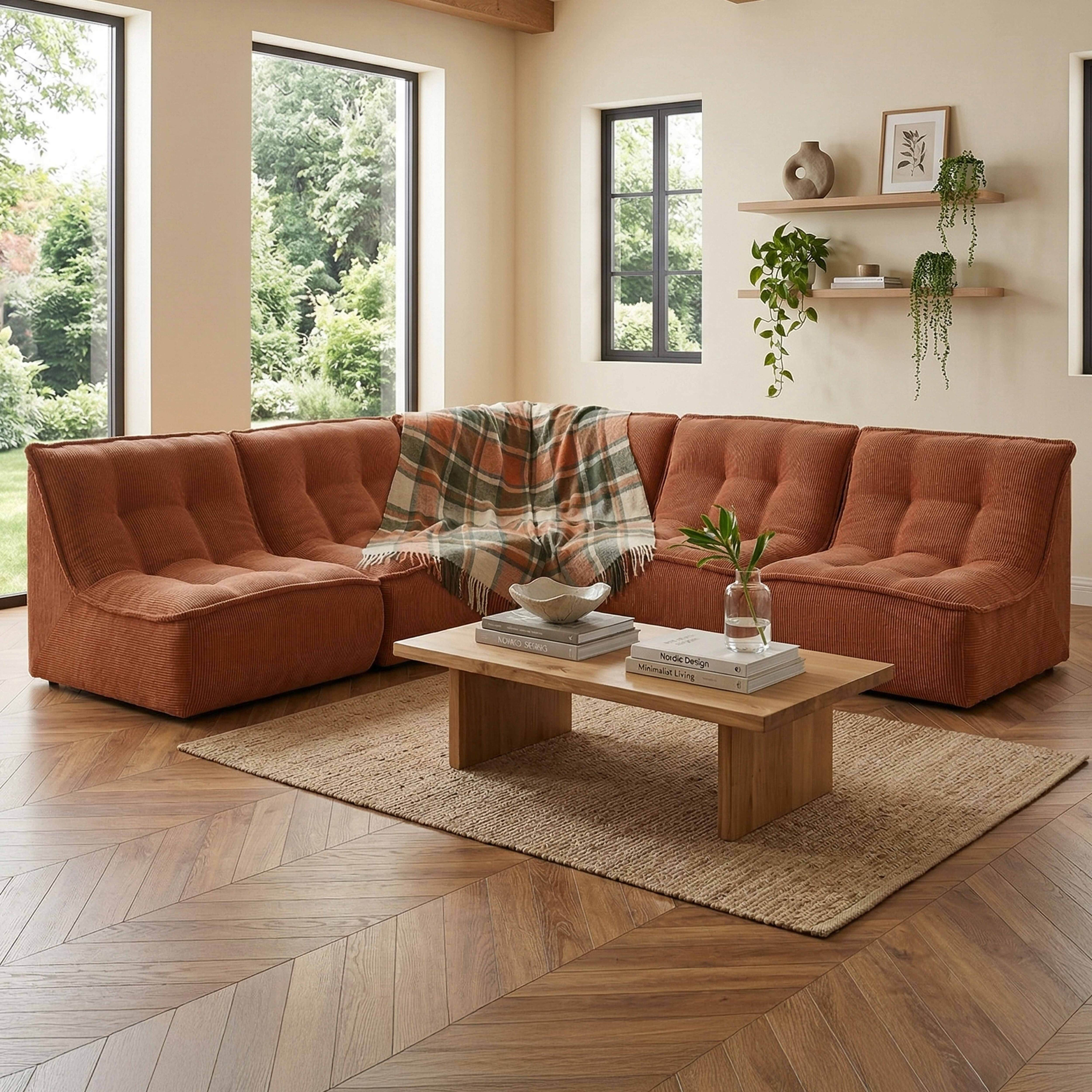 Ein orangefarbenes Ecksofa mit karierter Decke steht auf einem Teppich vor einem Holztisch.