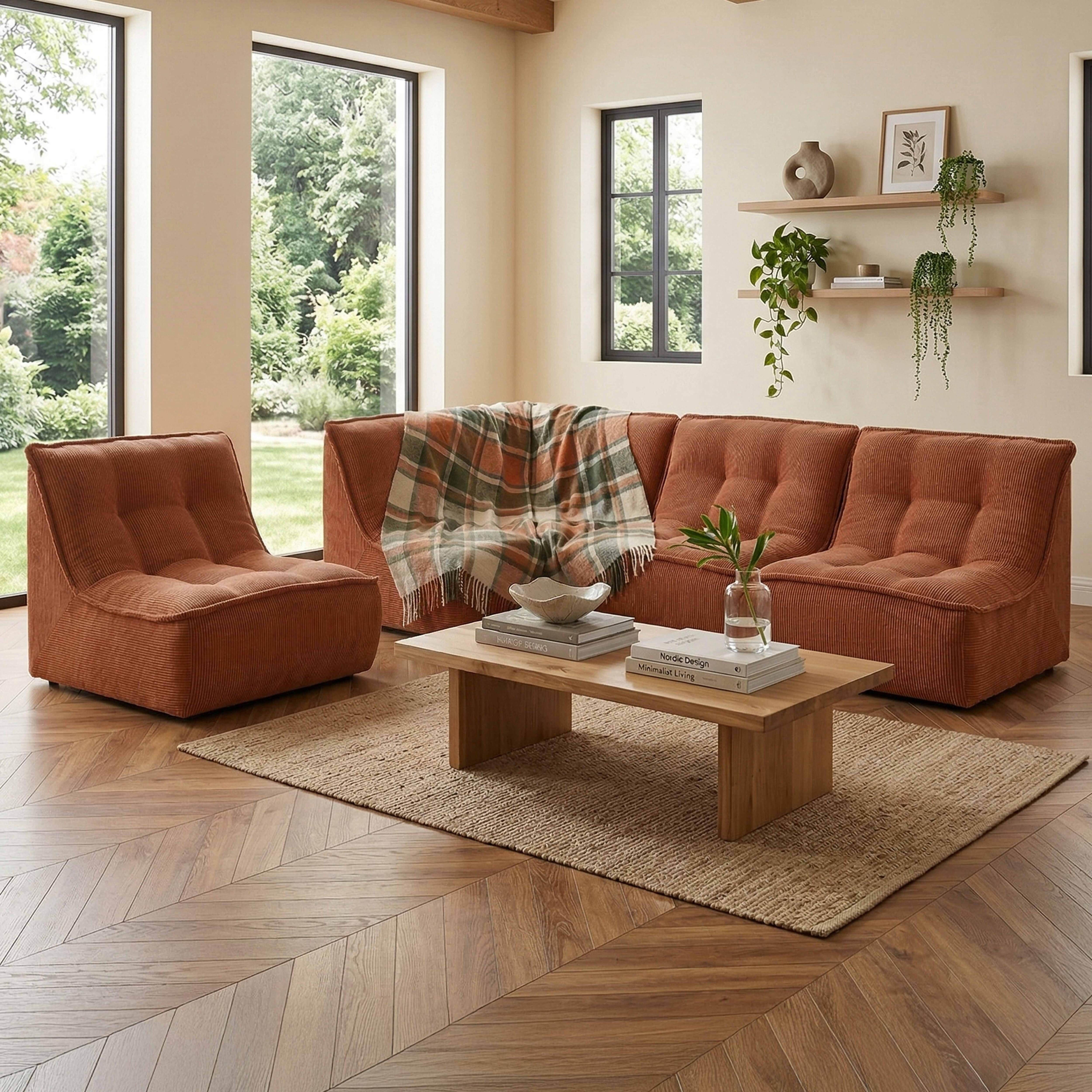 Ein orangefarbenes Cord-Sofa und ein Sessel stehen auf einem Teppich vor einem Holztisch mit Büchern.