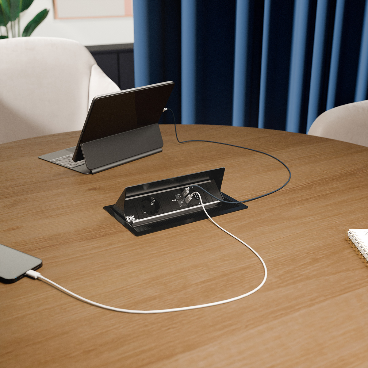 Ein Tablet und ein Handy laden über eine Pop-up-Stromleiste an einem Holztisch.