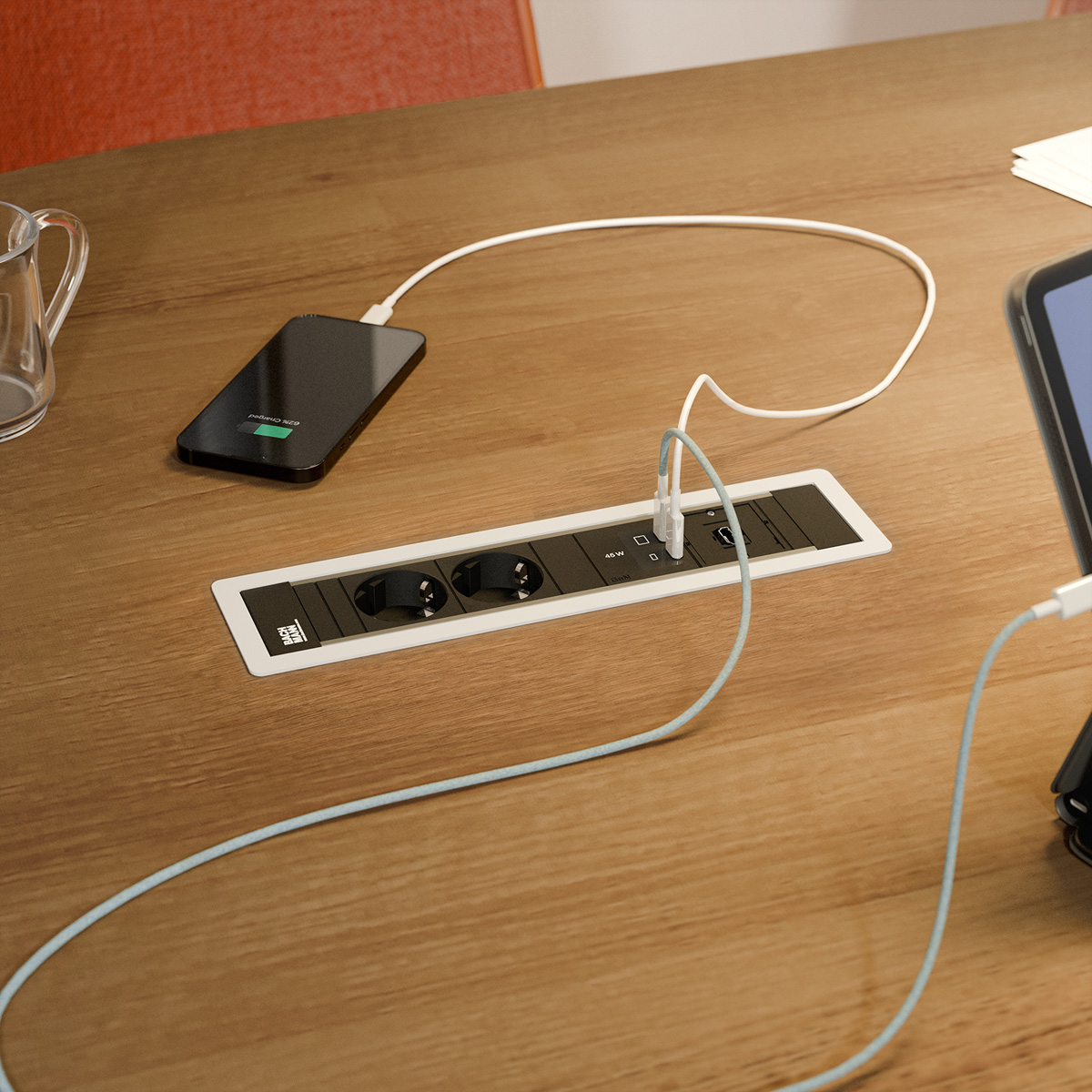 Ein Smartphone und ein Tablet laden an einer Tischsteckdose auf einem Holztisch.