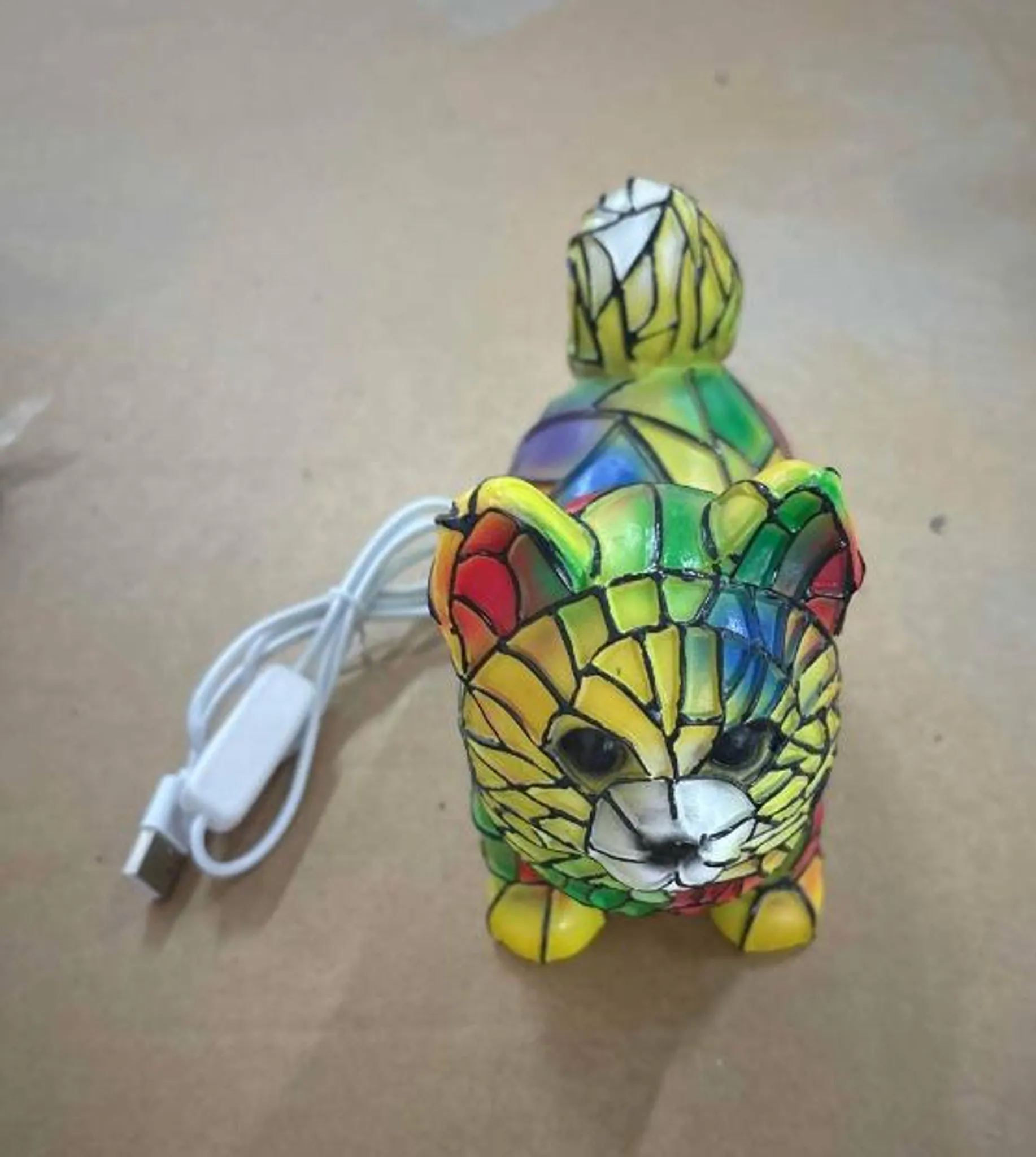 Eine bunte Katze-Lampe aus Glasmosaik mit einem weißen USB-Kabel.