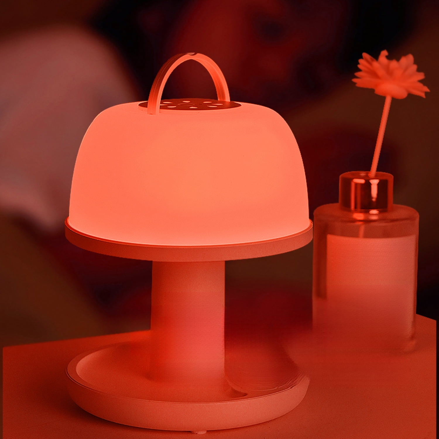 Eine orangefarbene Lampe mit Henkel steht neben einer Glasvase mit einer Blume.