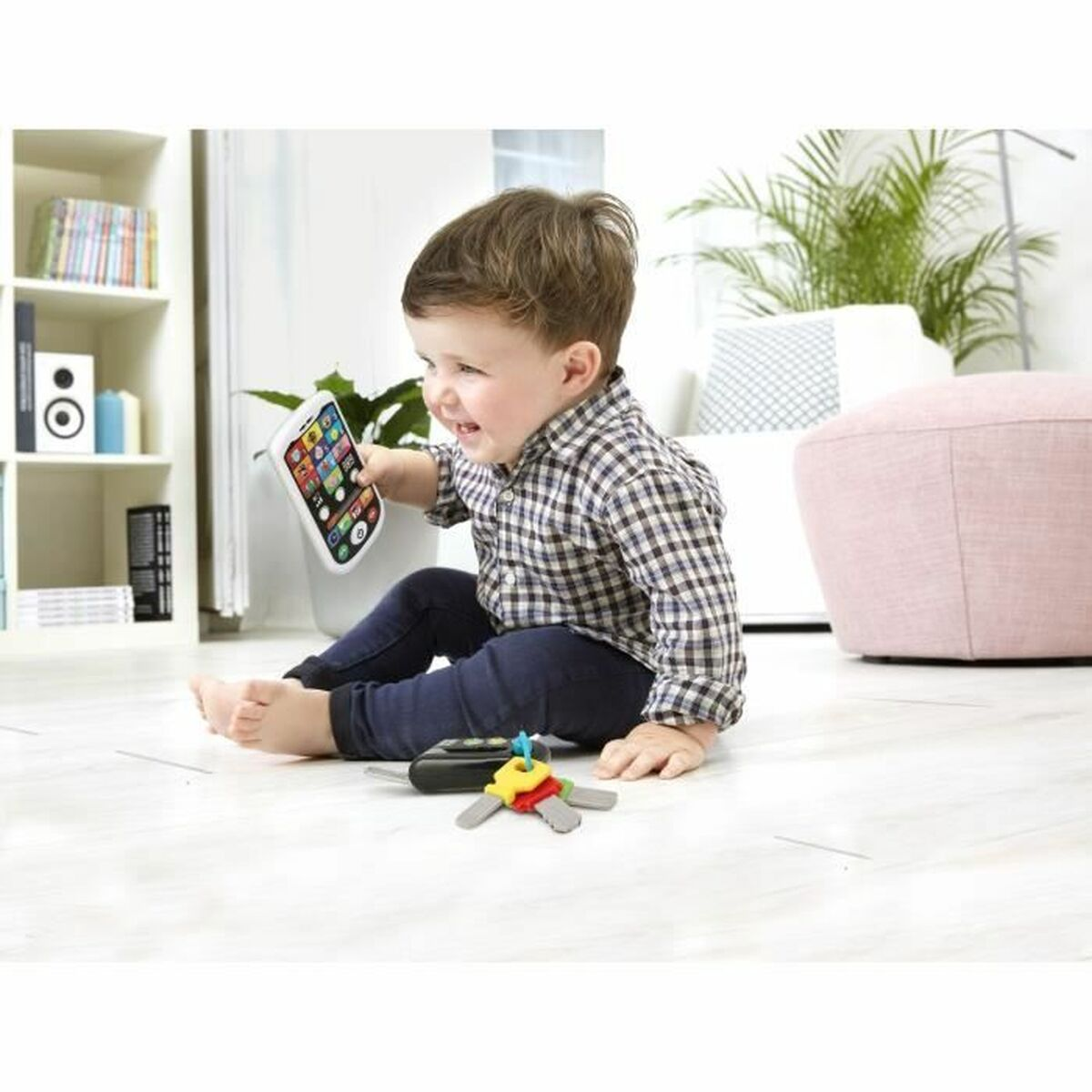 Ein Kleinkind sitzt auf dem Boden und hält ein Spielzeughandy. Spielzeugschlüssel liegen daneben.