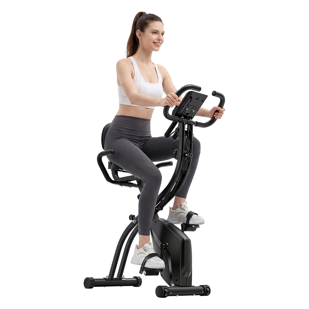 Frau in weißem Sportoberteil und grauer Hose auf einem schwarzen Heimtrainer.