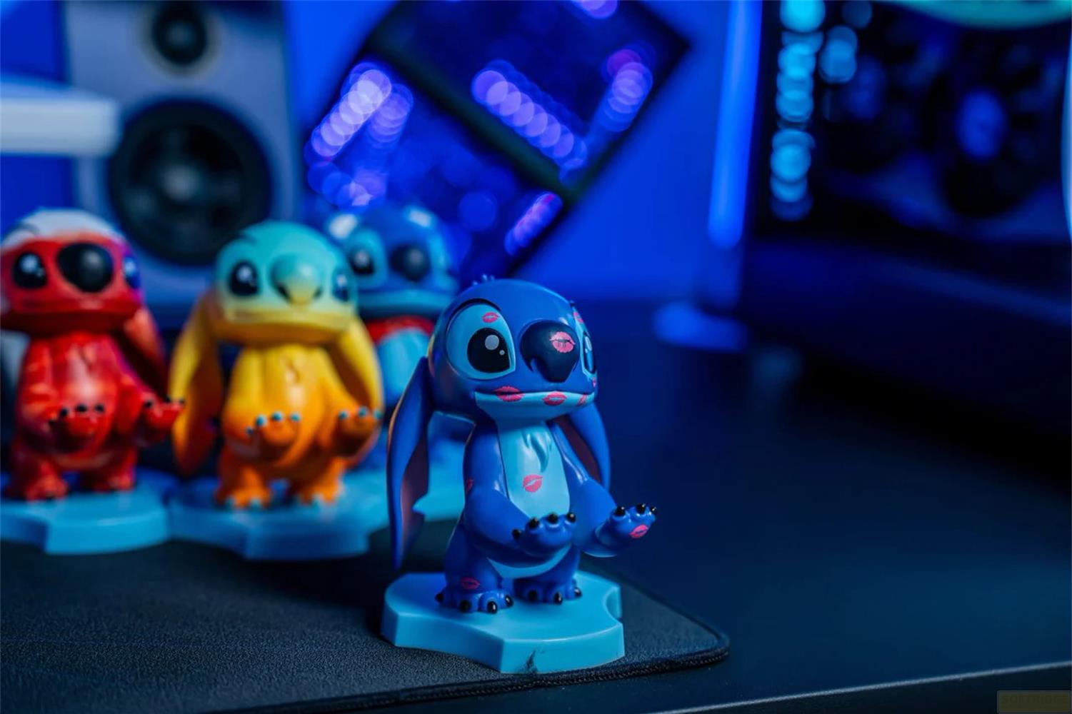 Quattro statuette di Stitch con baci di rossetto su una scrivania sotto luci blu.