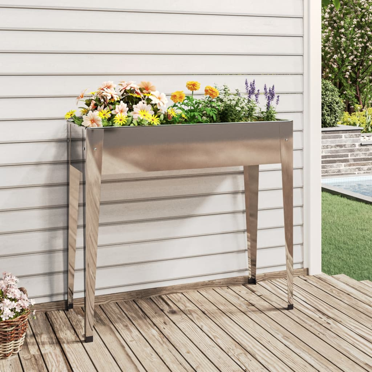 Ein glänzender Metallpflanzer mit bunten Blumen auf einer Holzterrasse.