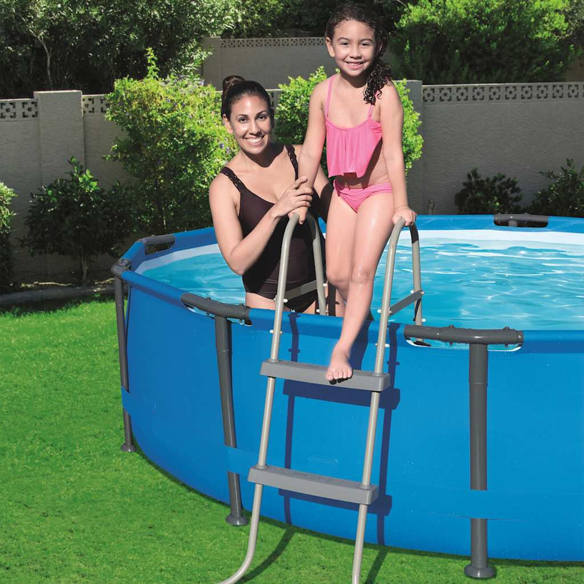 Frau und Mädchen in Badeanzügen steigen aus einem blauen Pool über eine Leiter.