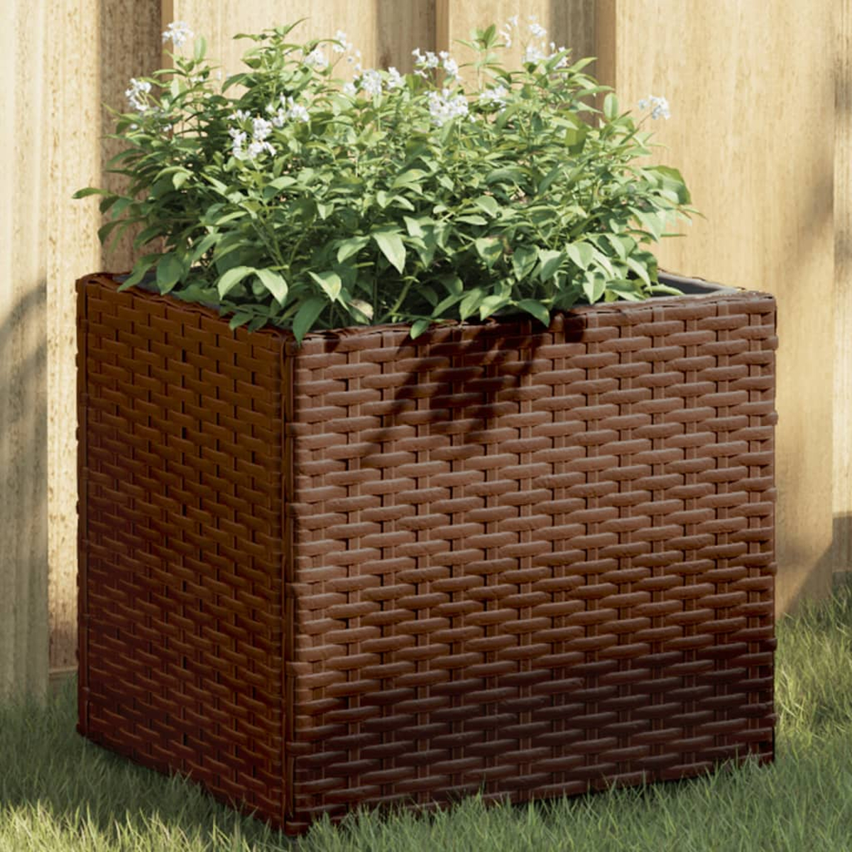 Fioriera marrone in rattan con piante verdi e fiori bianchi, sull'erba.