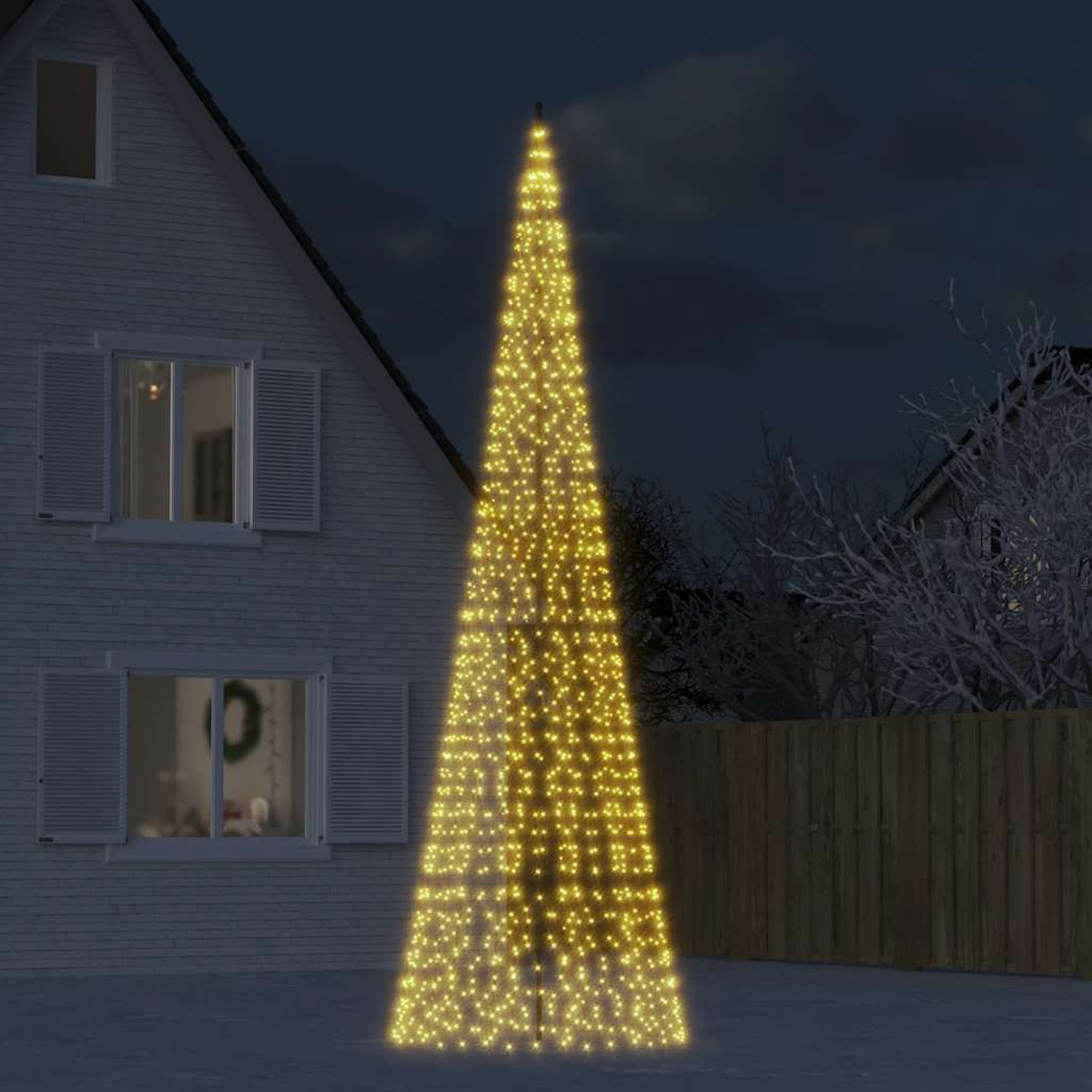 Ein hoher, beleuchteter Baum mit gelben Lichtern vor einem Haus im Dunkeln.