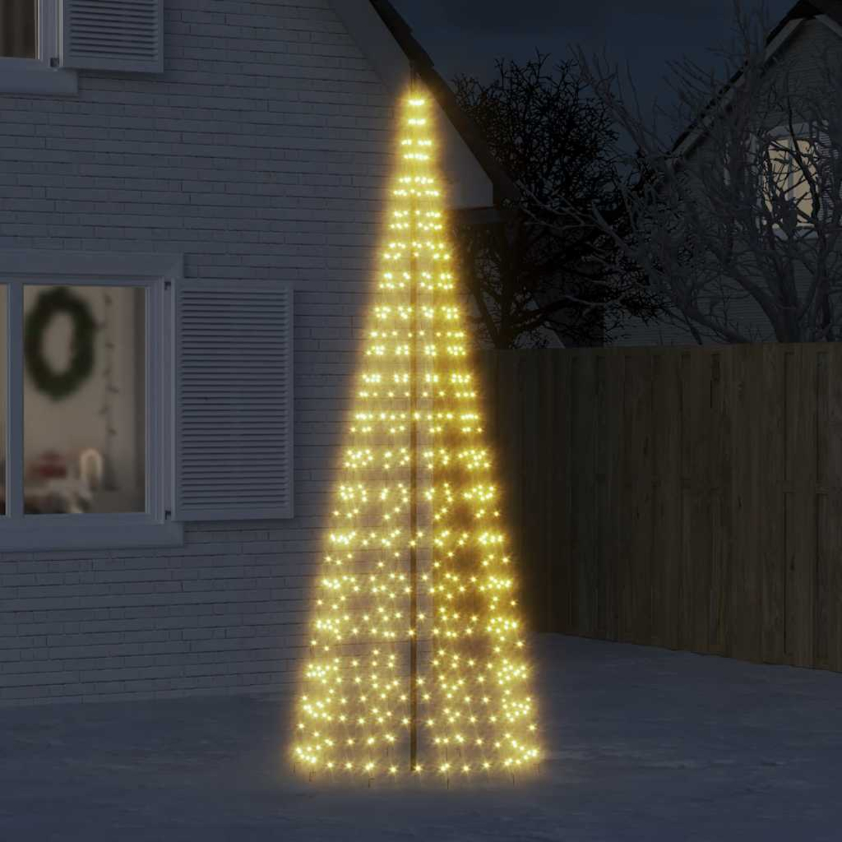 Ein konischer Weihnachtsbaum aus Lichtern steht im Schnee neben einem Haus.