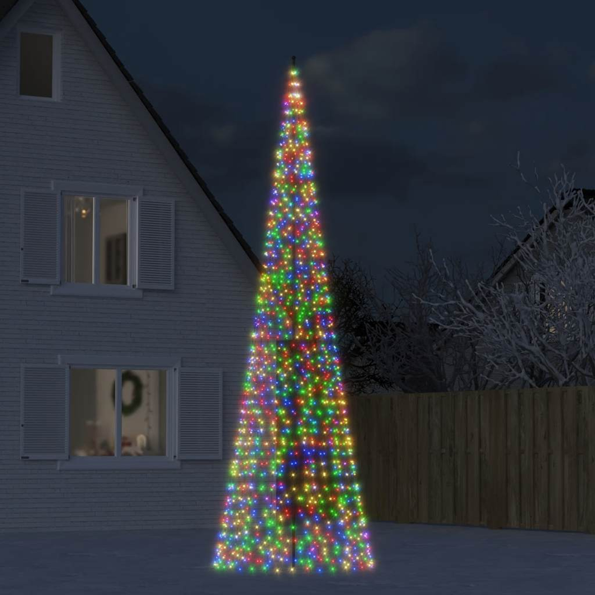 Ein beleuchteter, kegelförmiger Weihnachtsbaum mit bunten Lichtern steht vor einem Haus im Dunkeln.